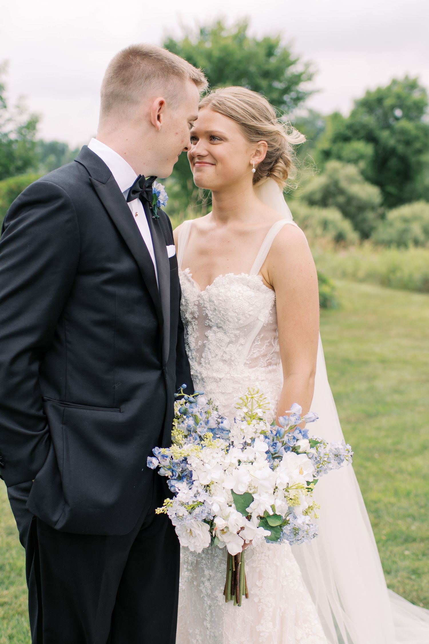 Close-up wedding photos showing a beautiful bouquet with blue and white flowers against formal attire.