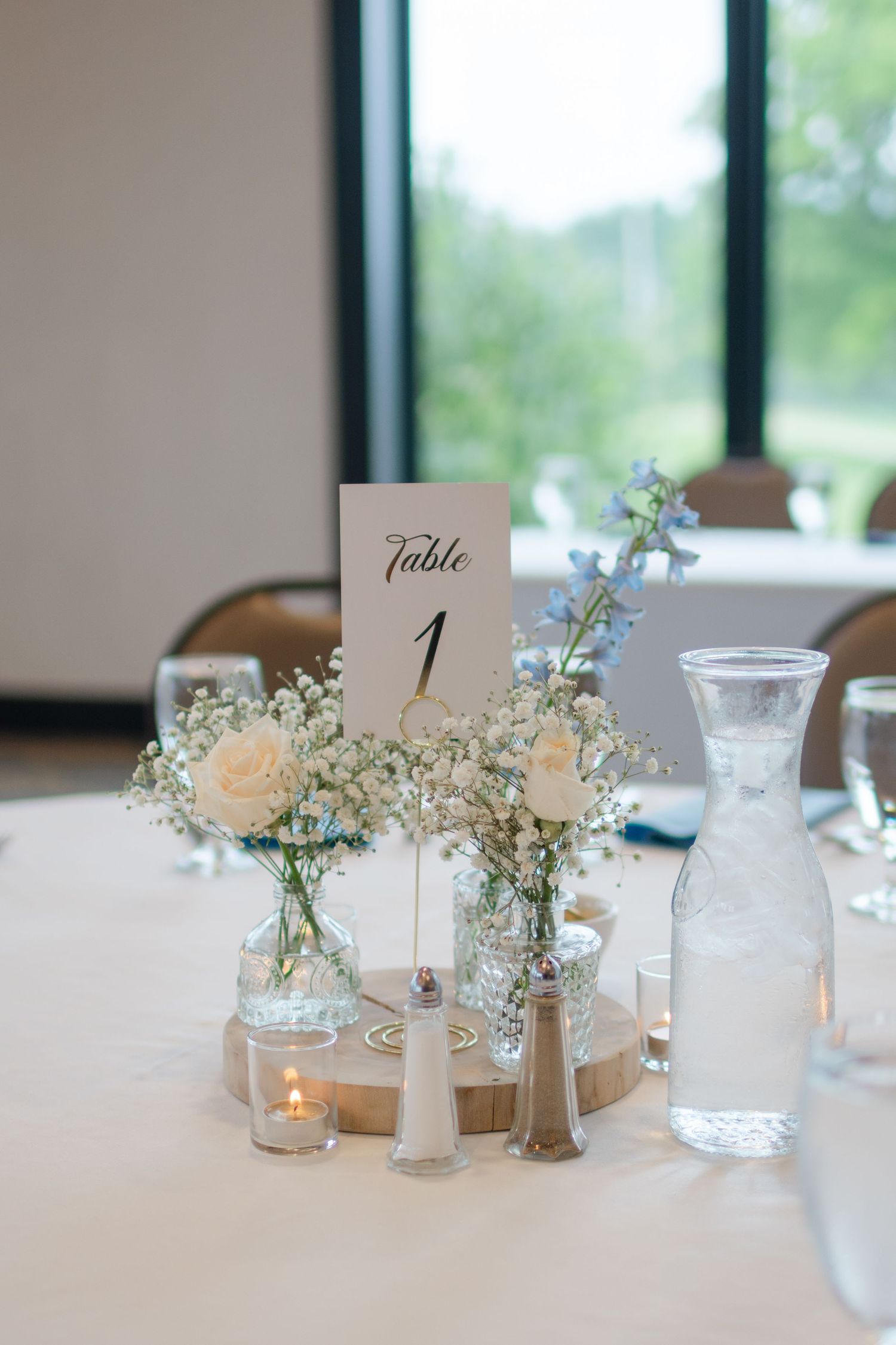 Elegant wedding centerpiece featuring table number one with delicate white flowers and blue accents in glass vases.