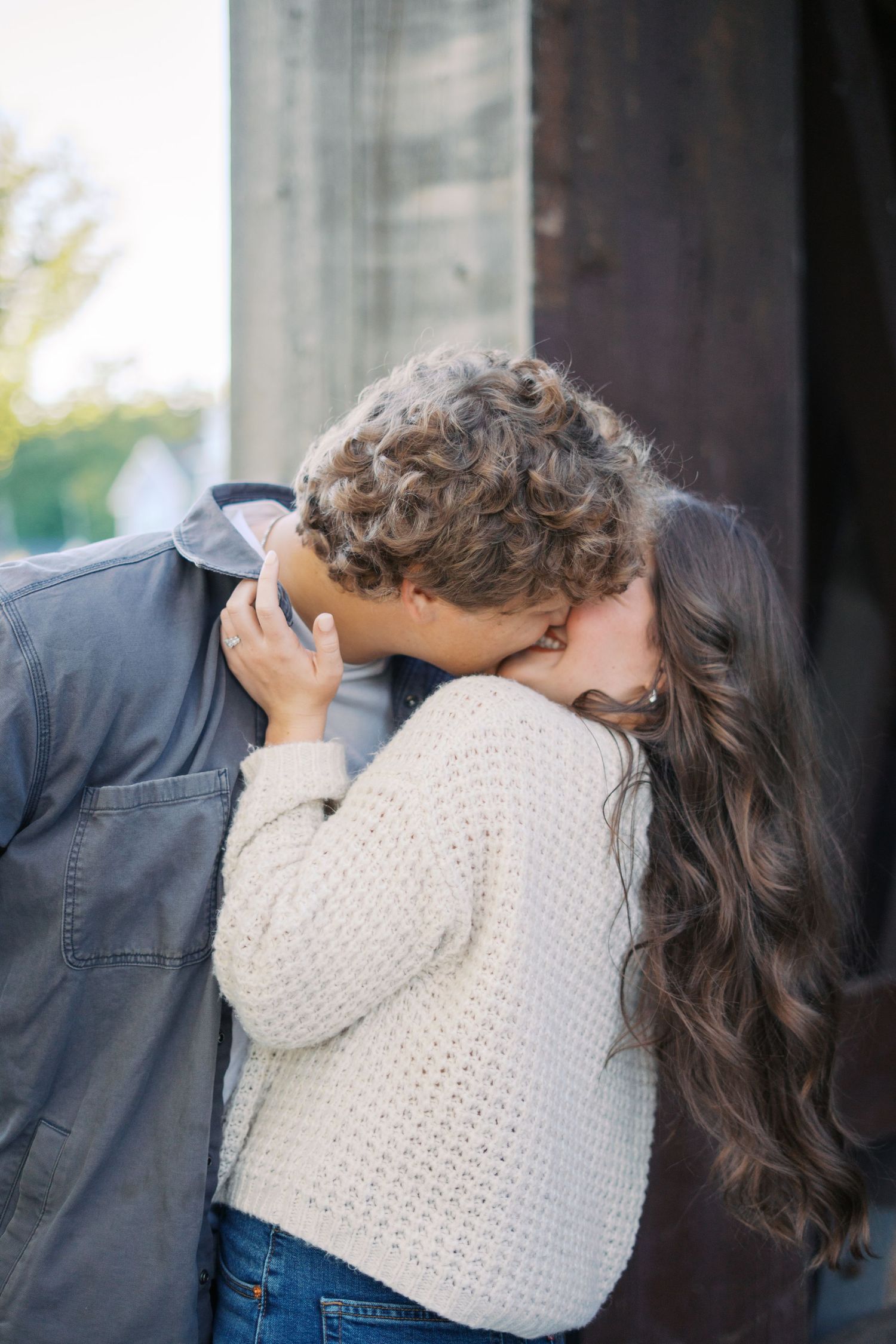 Couple embracing tenderly under wooden beams in natural lighting.