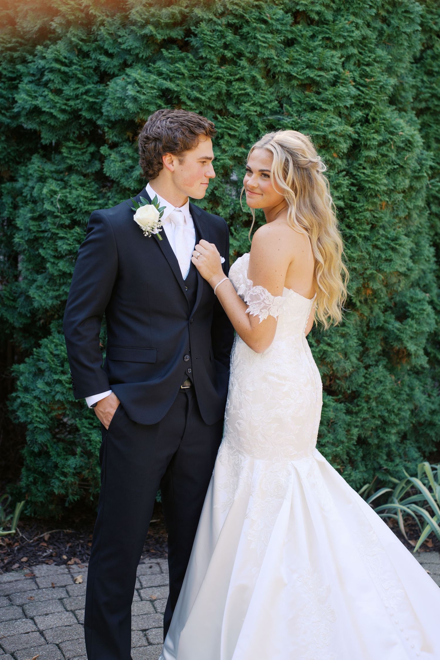 A couple shares a playful moment during their wedding photoshoot against a backdrop of green foliage.
