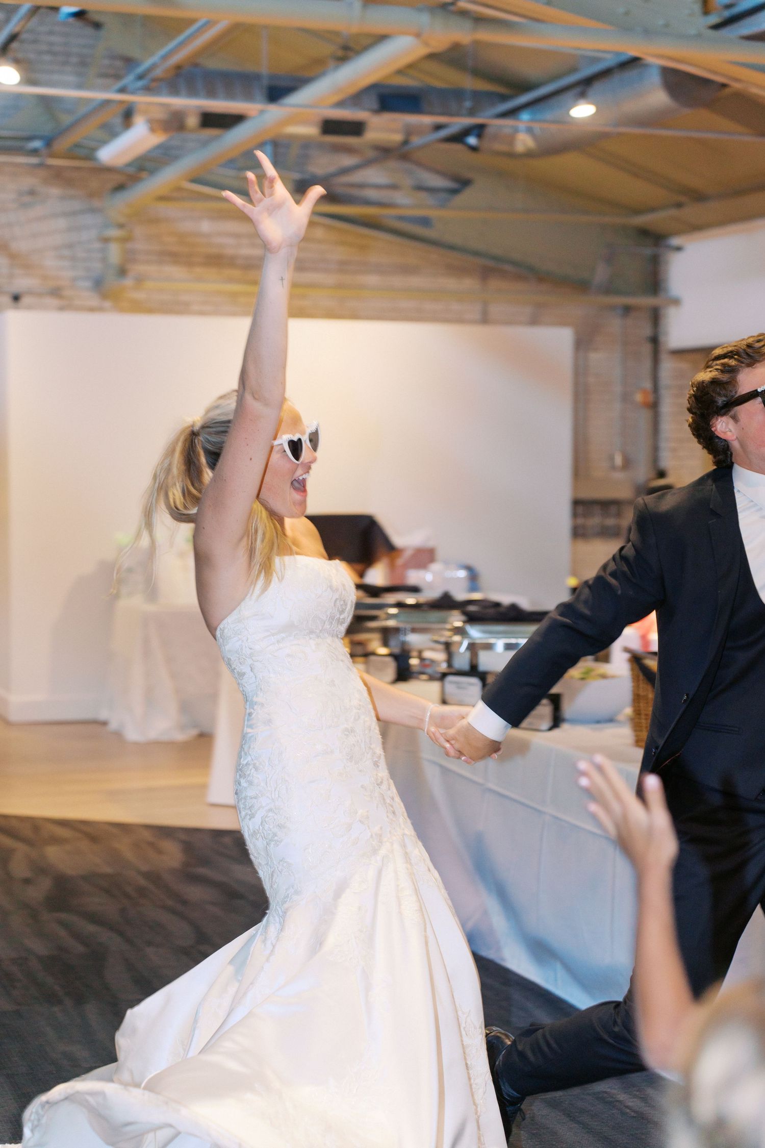 A couple performs energetic dance moves in an industrial-style wedding venue.