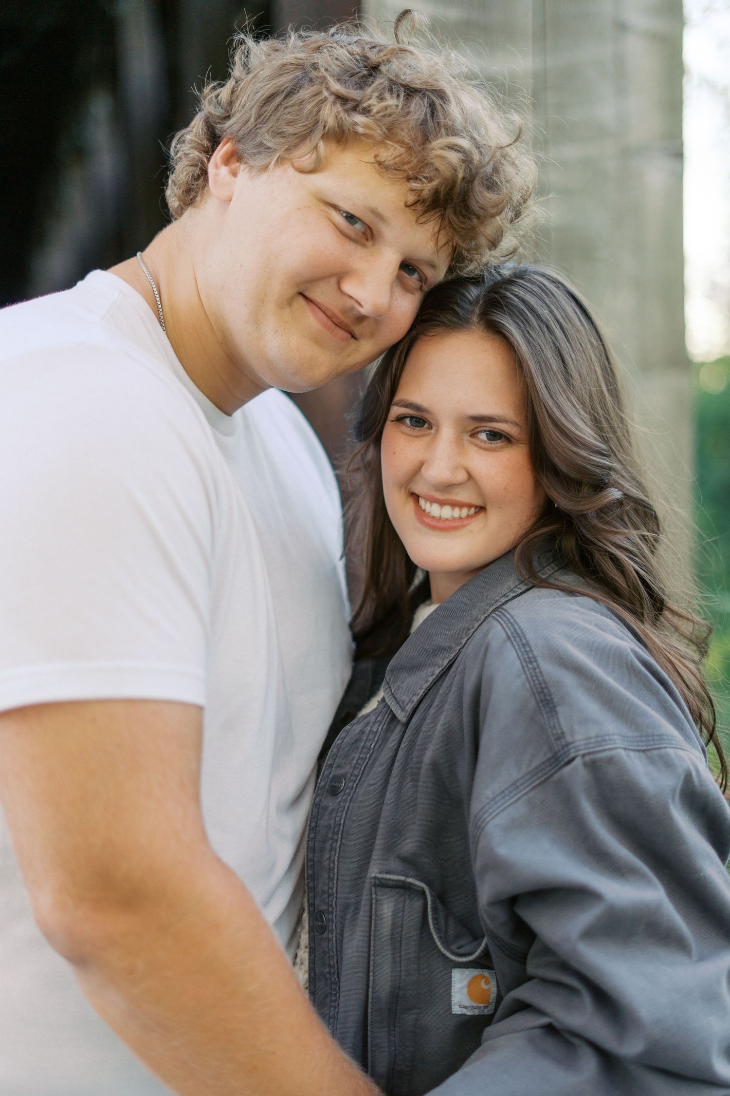 Couple in casual attire sharing affectionate moments against an industrial backdrop.