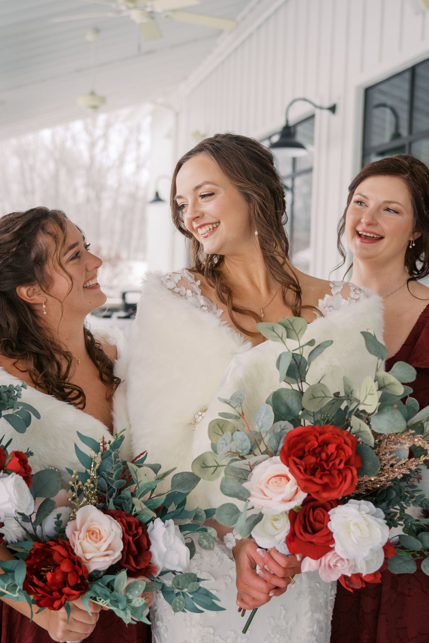 Bridesmaids in burgundy dresses holding white and red bouquets with eucalyptus.