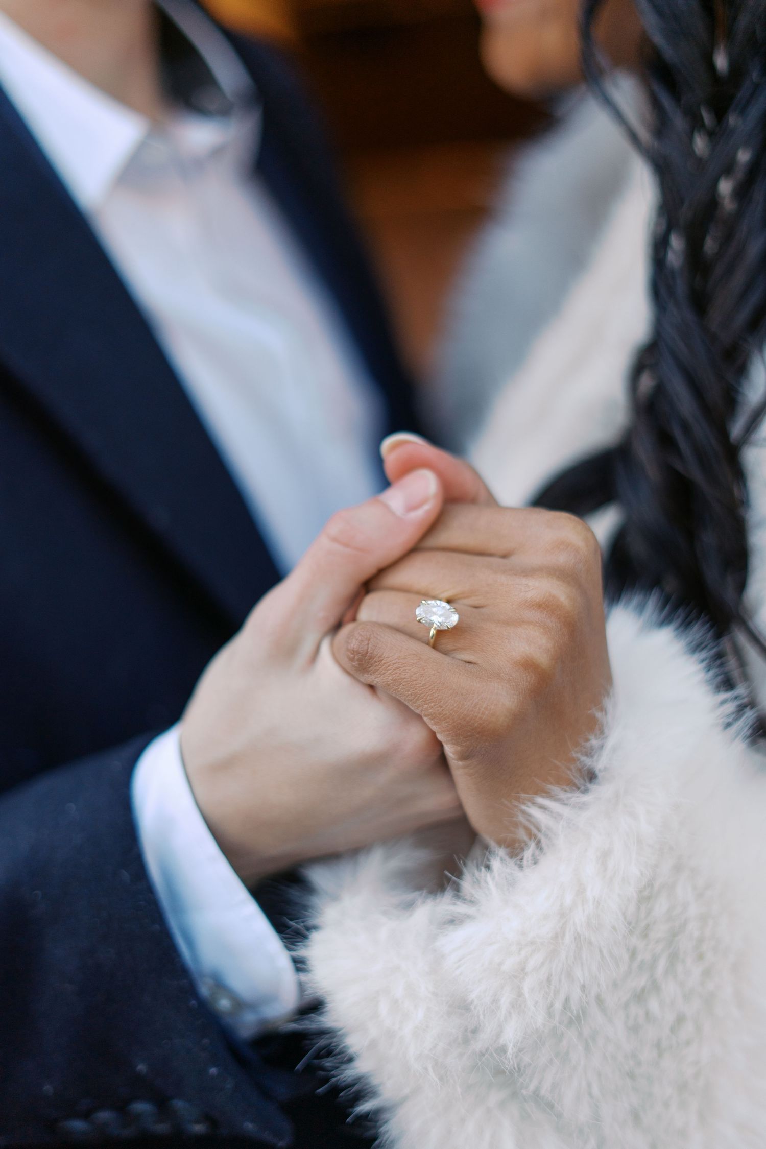 Close-up of clasped hands showing an engagement ring against winter formal attire.