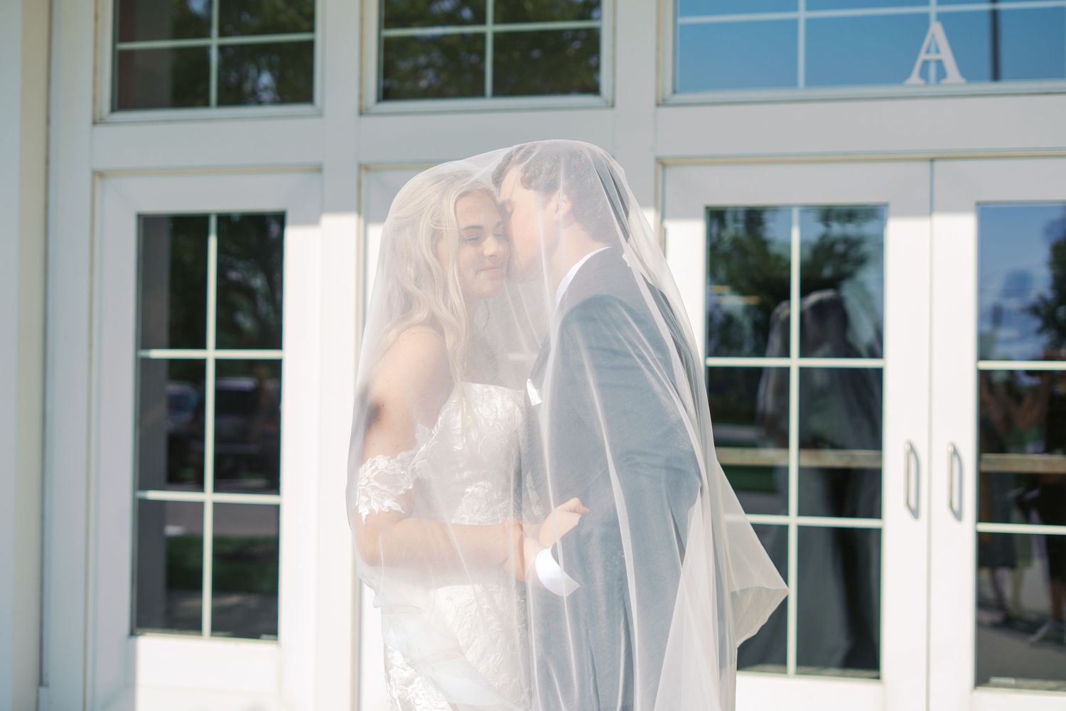 Romantic veiled portrait of couple sharing tender moment against white doors.