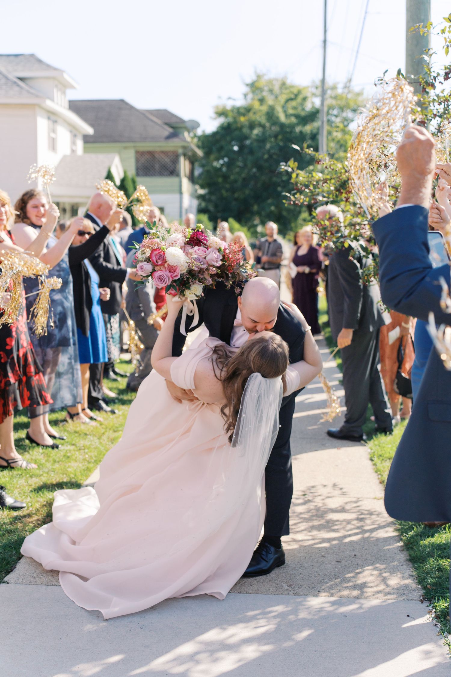Wedding guests celebrate as a couple dances in a blush pink gown and formal attire at an outdoor venue.