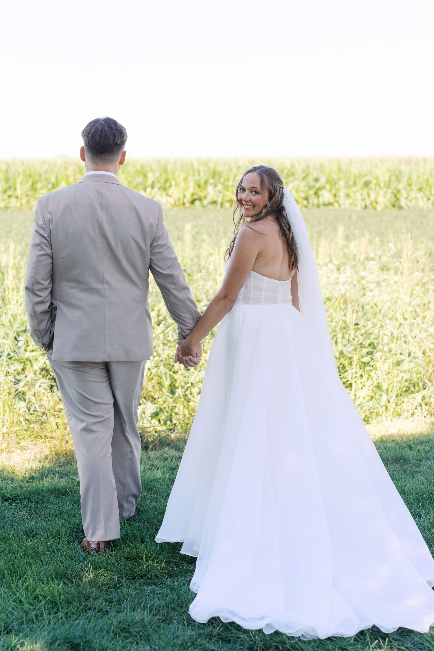 Newlyweds walk through a grassy field together during their wedding photo session.