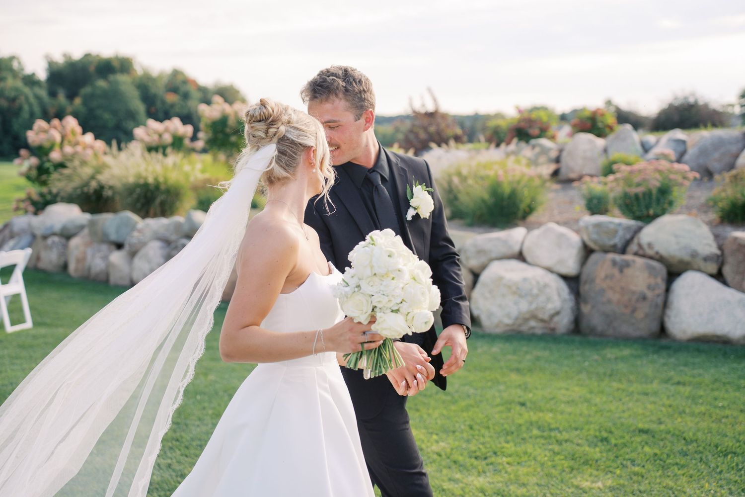 Elegant wedding couple embracing outdoors with natural stone landscaping in background.