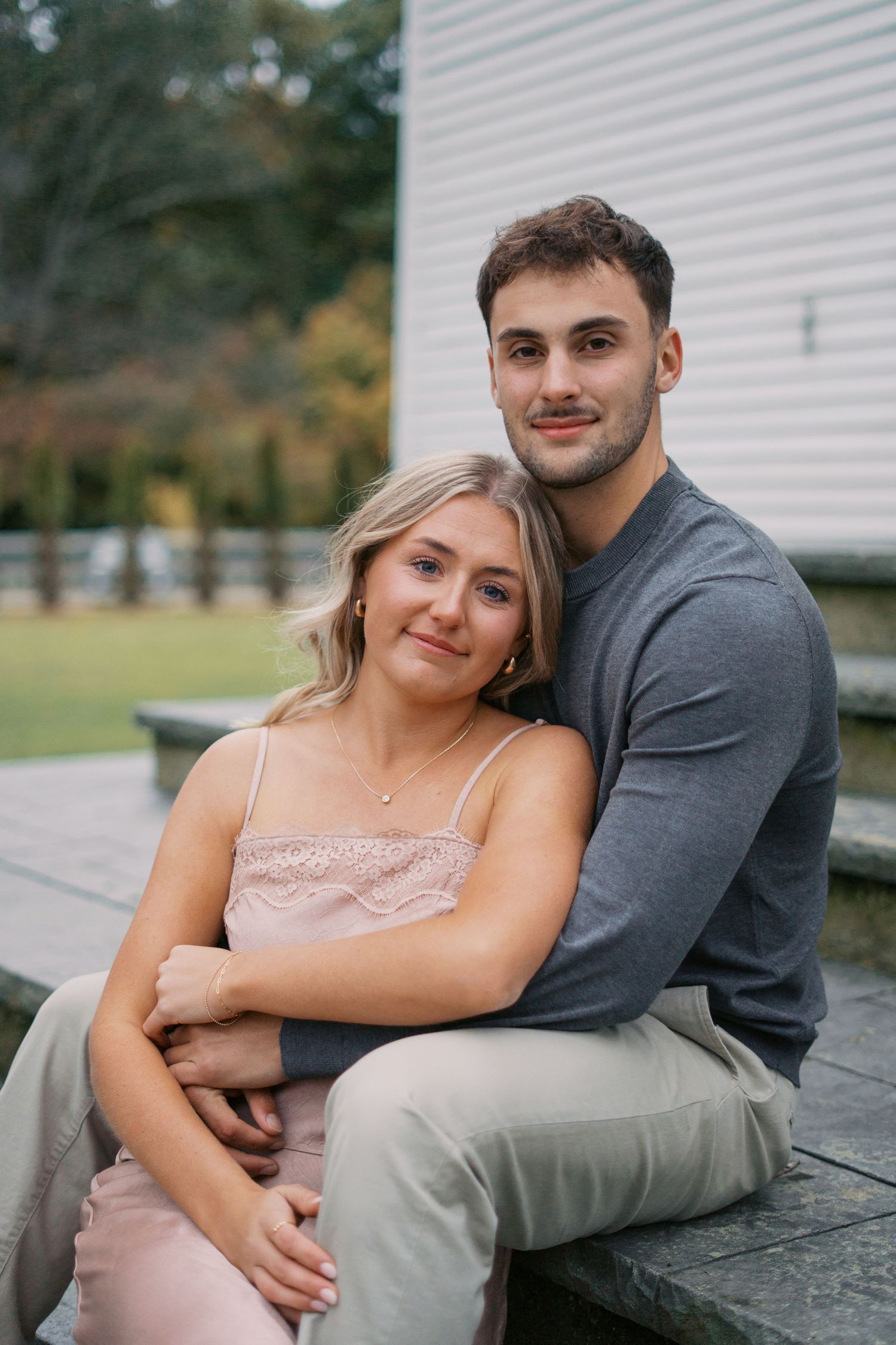 Couple shares intimate moments during outdoor photo session near white building.