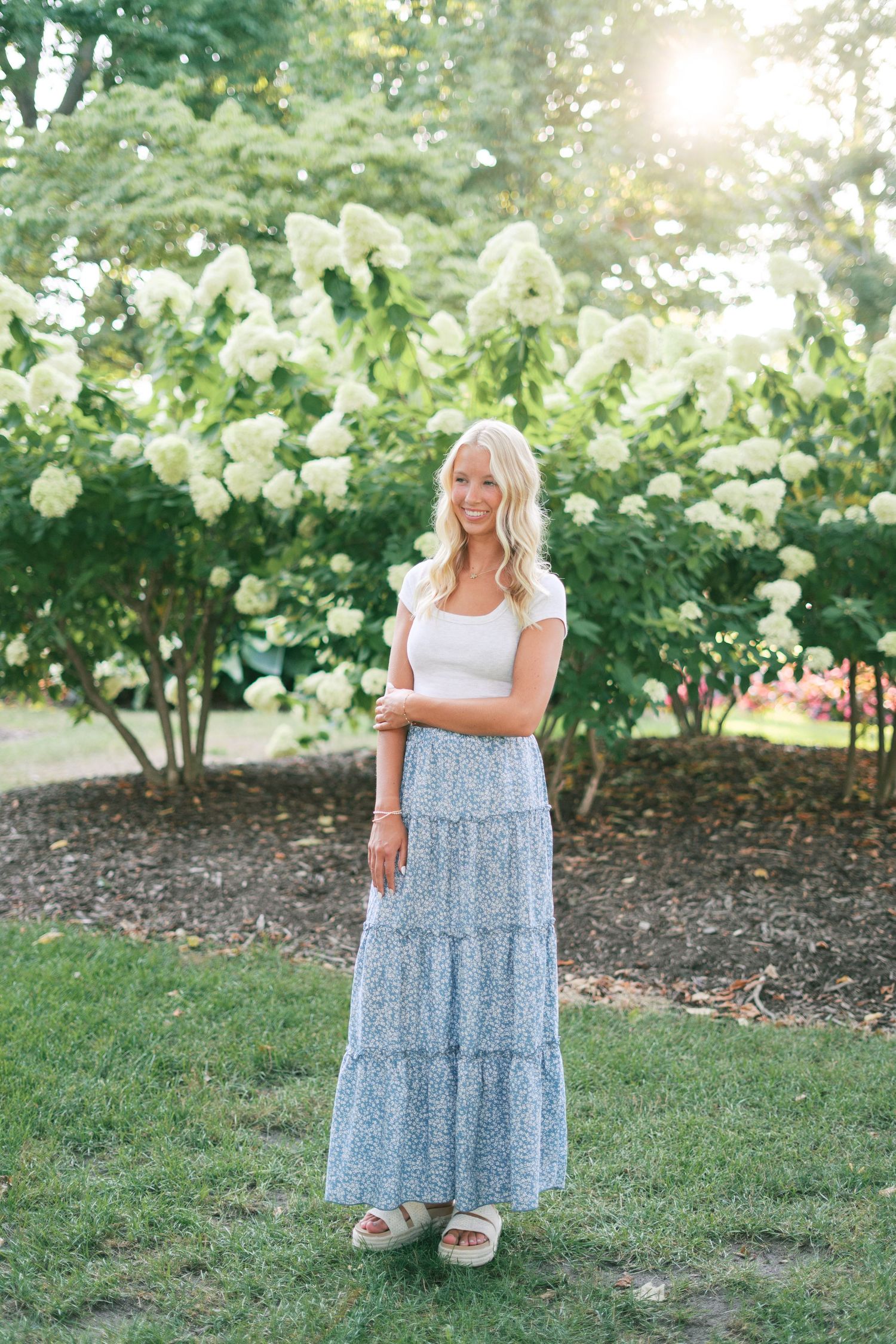 Portrait session in tiered floral dress against garden landscape.