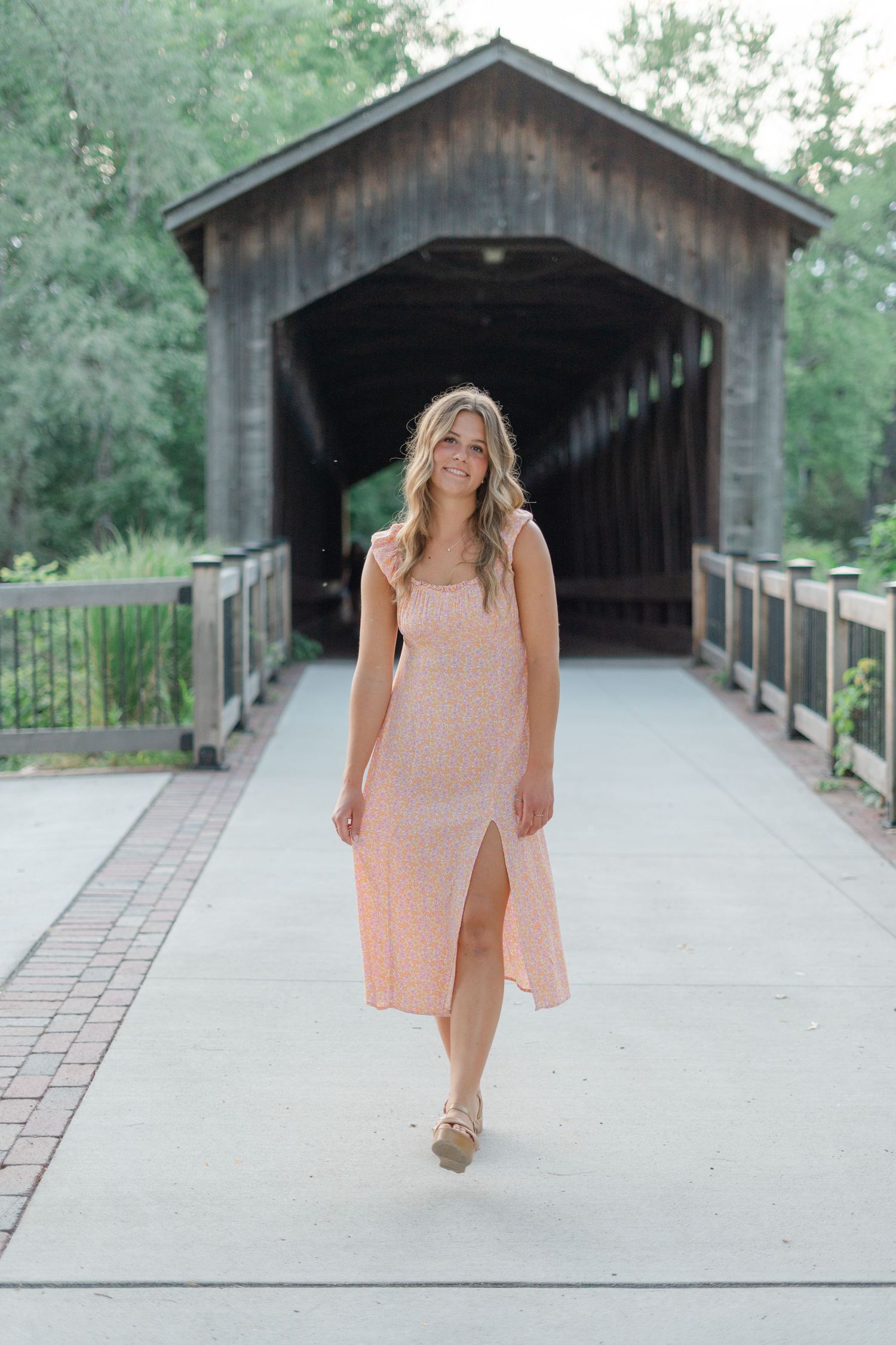 Walking portrait at a covered bridge entrance in a pink summer dress.