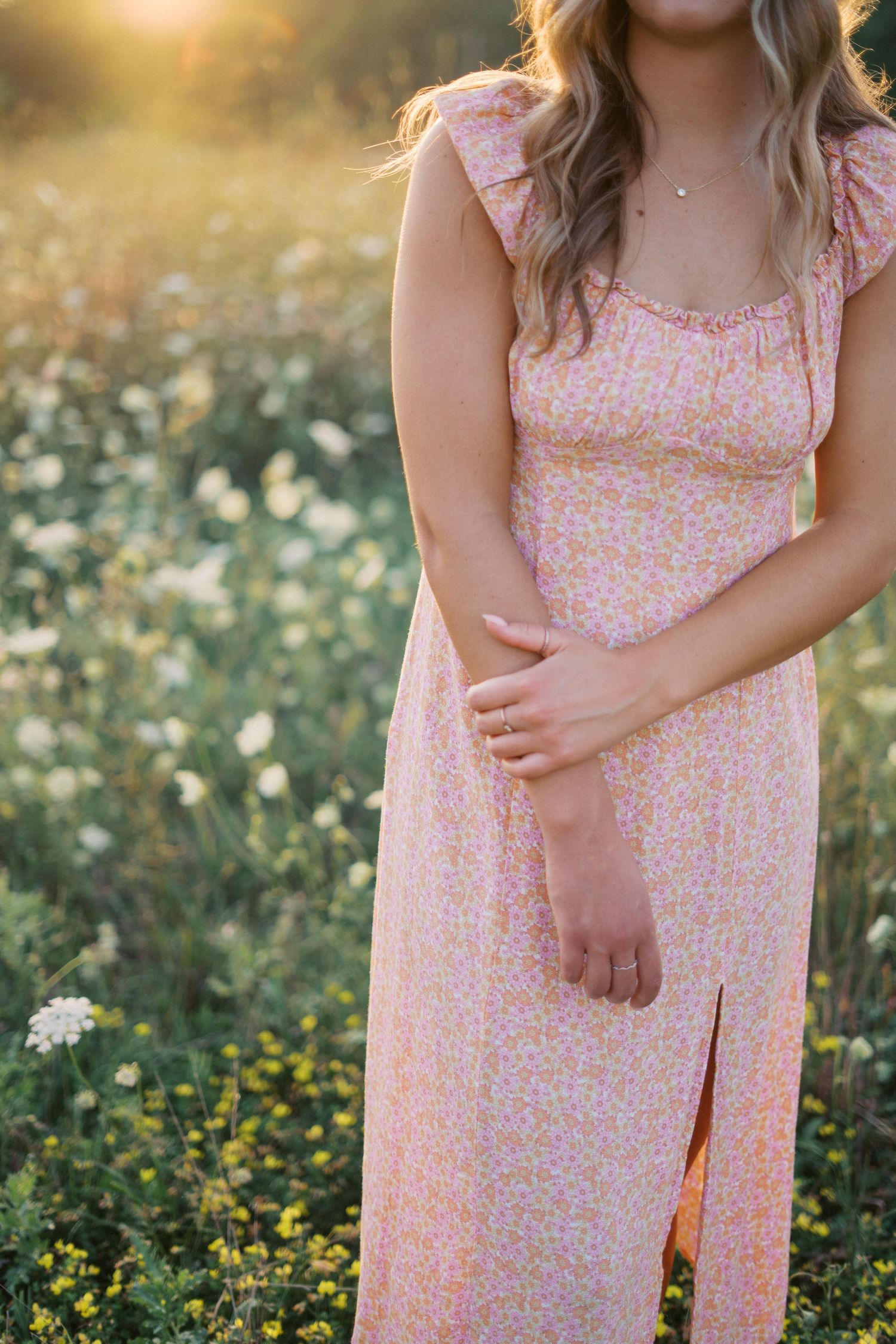 Close-up detail of a pink floral sundress with ruffle sleeves in a golden meadow at sunset.
