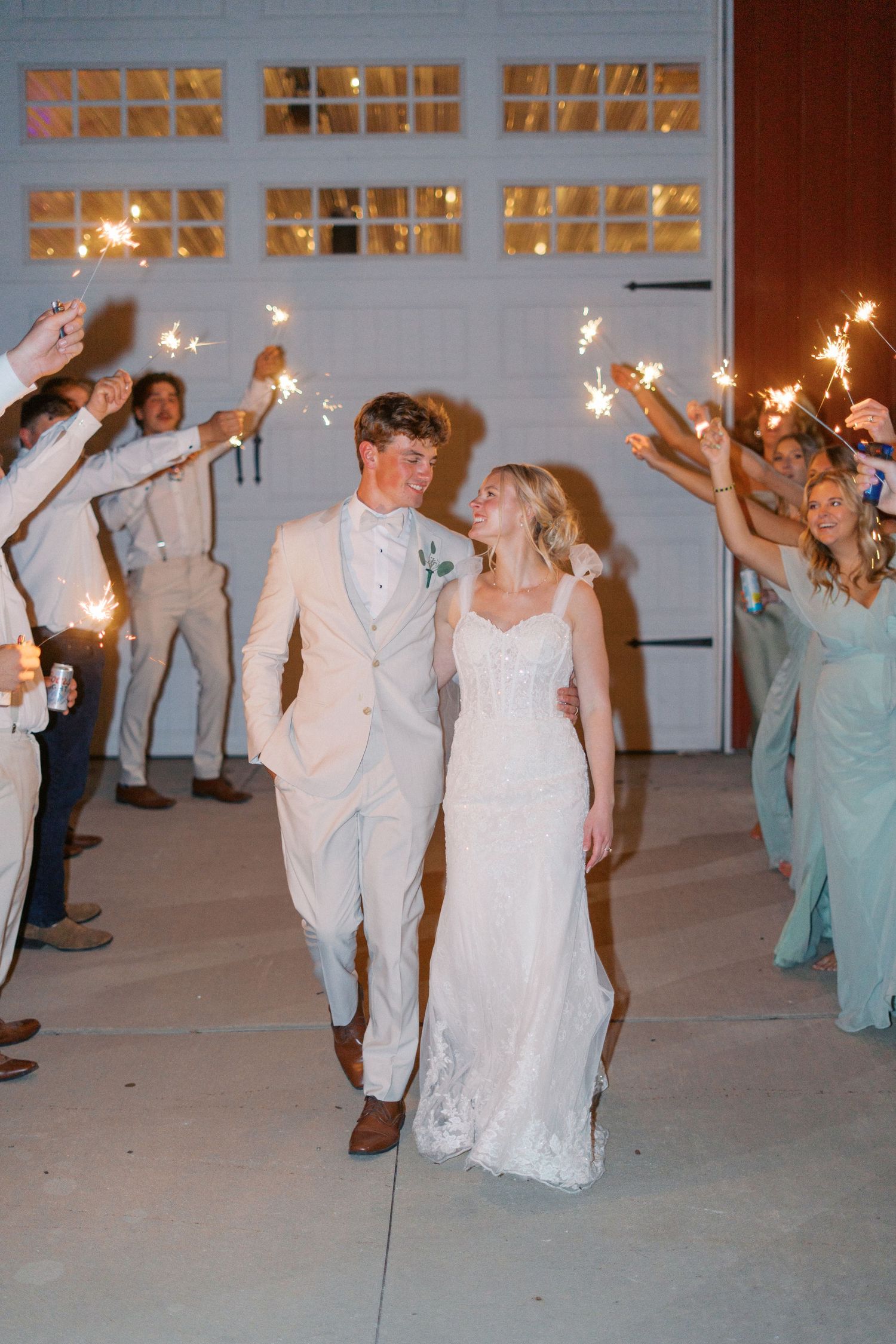 Wedding party dances with sparklers during an evening celebration in front of a white building.