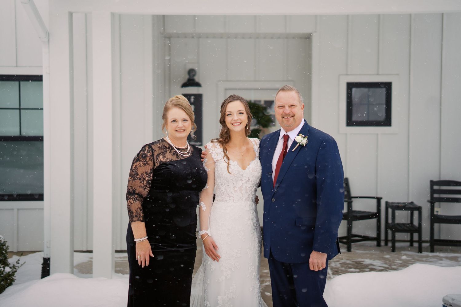 Wedding party poses together outdoors against white building in winter setting.