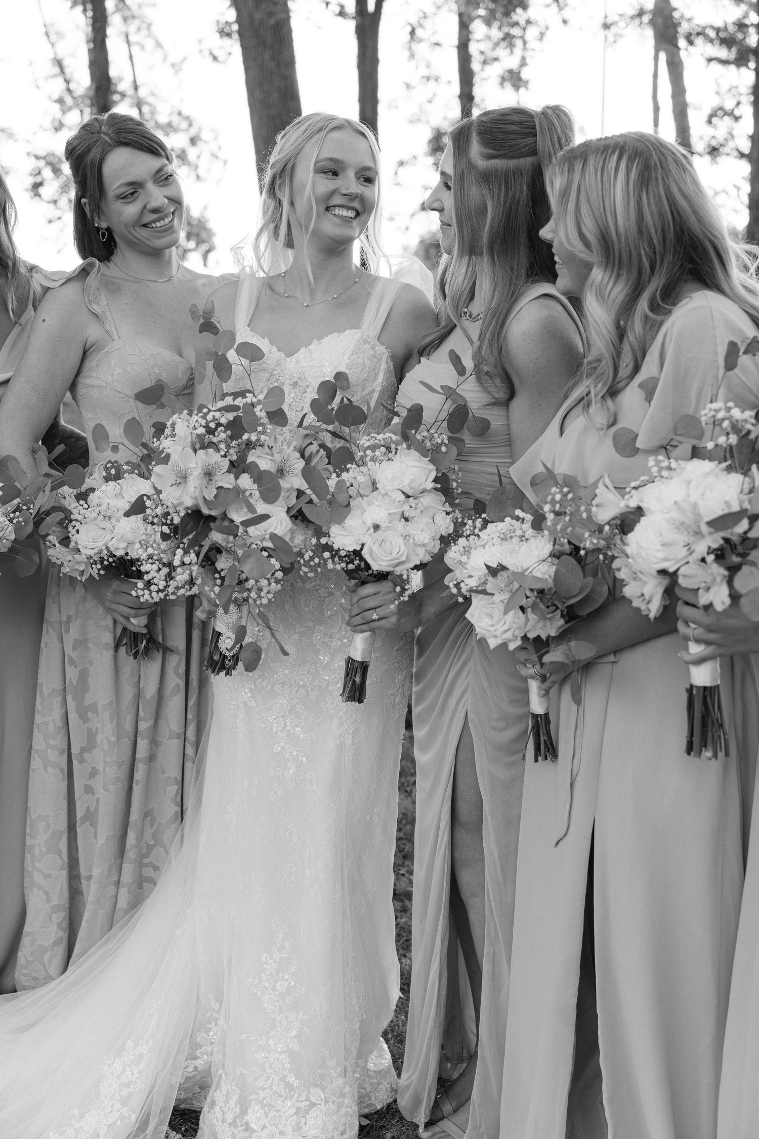 Wedding party holds elegant white floral bouquets in a black and white photo.