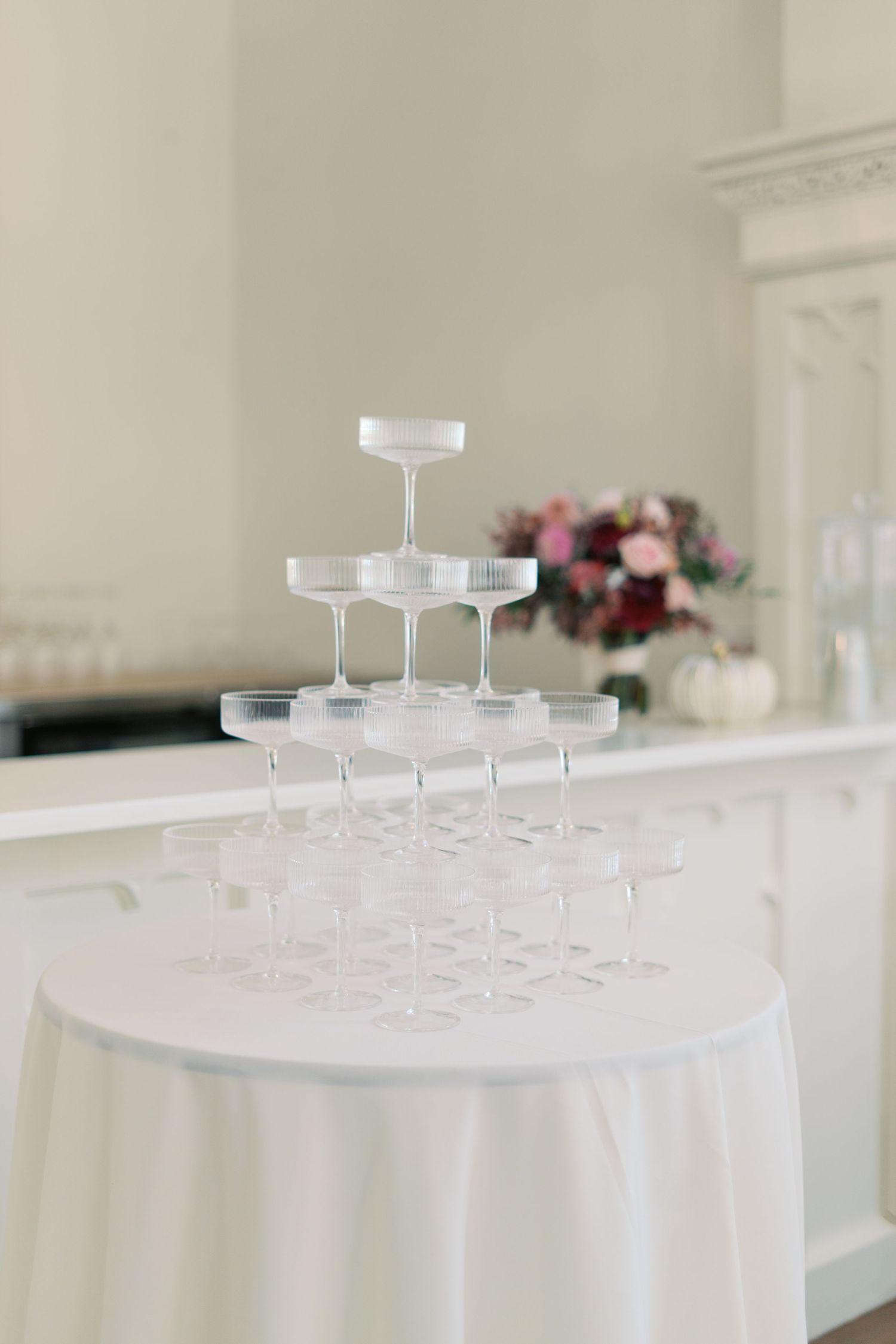 Empty champagne glasses arranged in a pyramid tower on a white tablecloth at an elegant event setting.