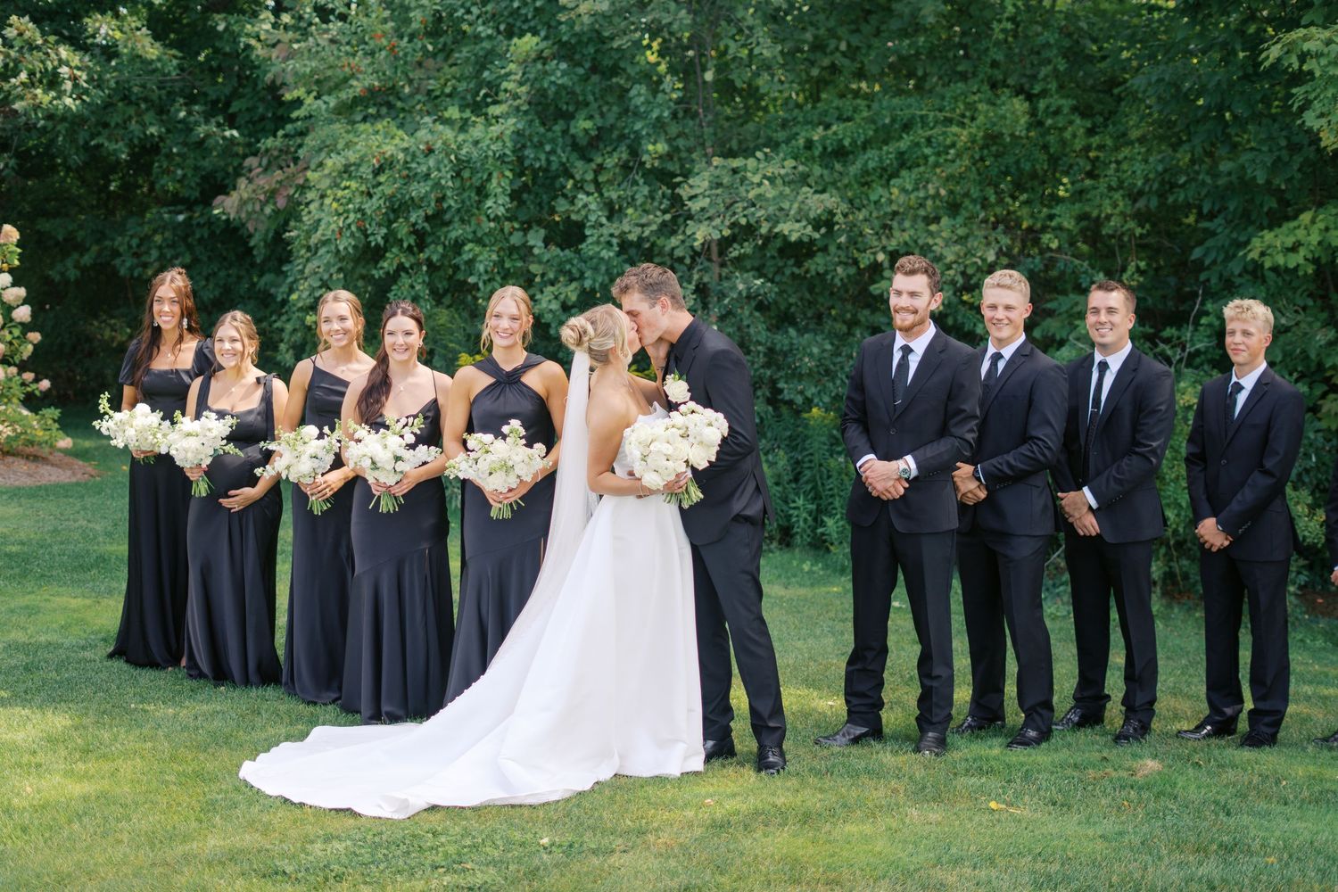 Wedding party in navy and white attire poses on green lawn during outdoor ceremony.