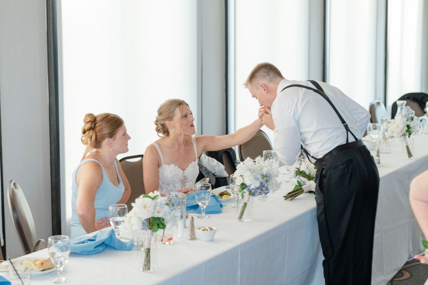 Wedding party members seated at a decorated head table with blue and white floral centerpieces.