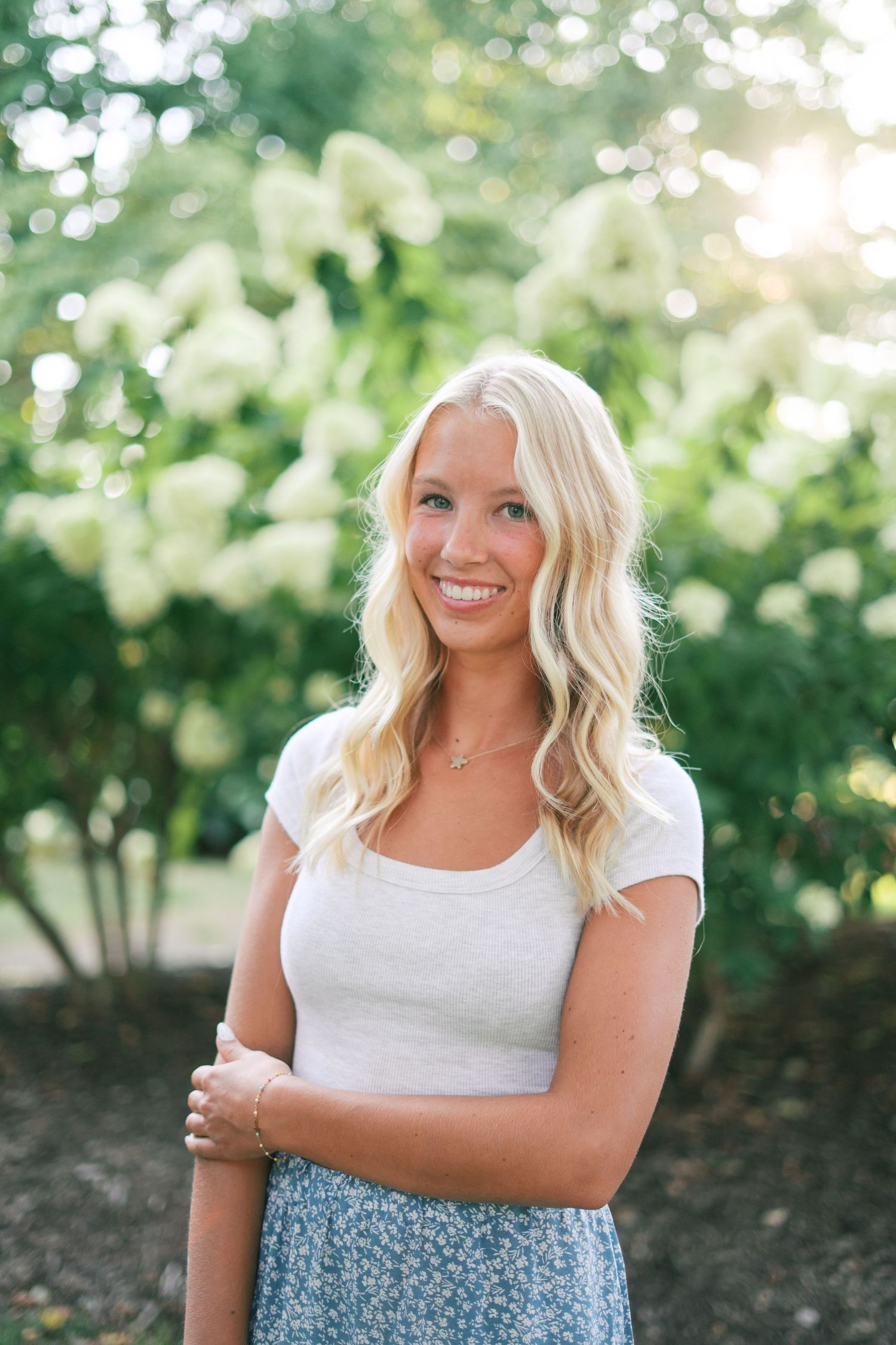 Portrait in a garden setting wearing white top against blooming flowers.