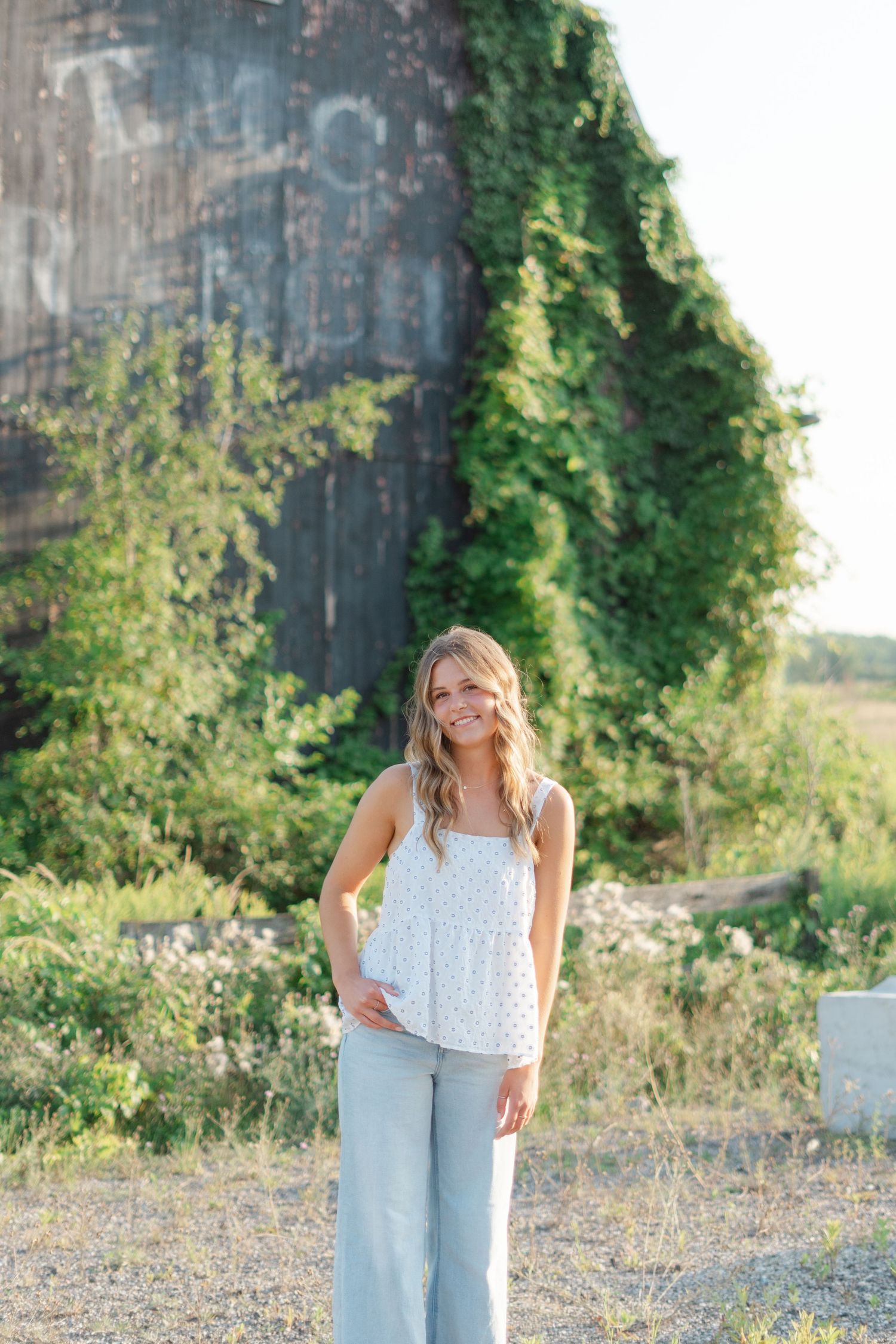 Casual outdoor portraits in light denim and white top near an old barn structure.
