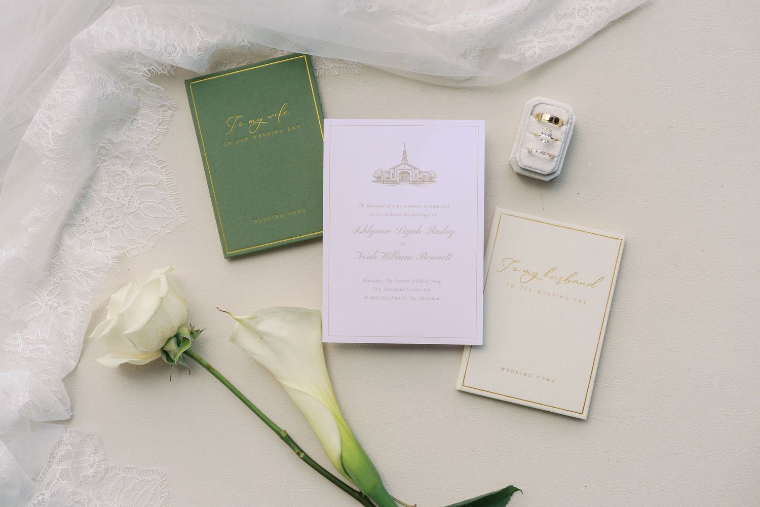 Elegant wedding stationery suite with gold details, white calla lily, ring box, and green accents on a neutral background.