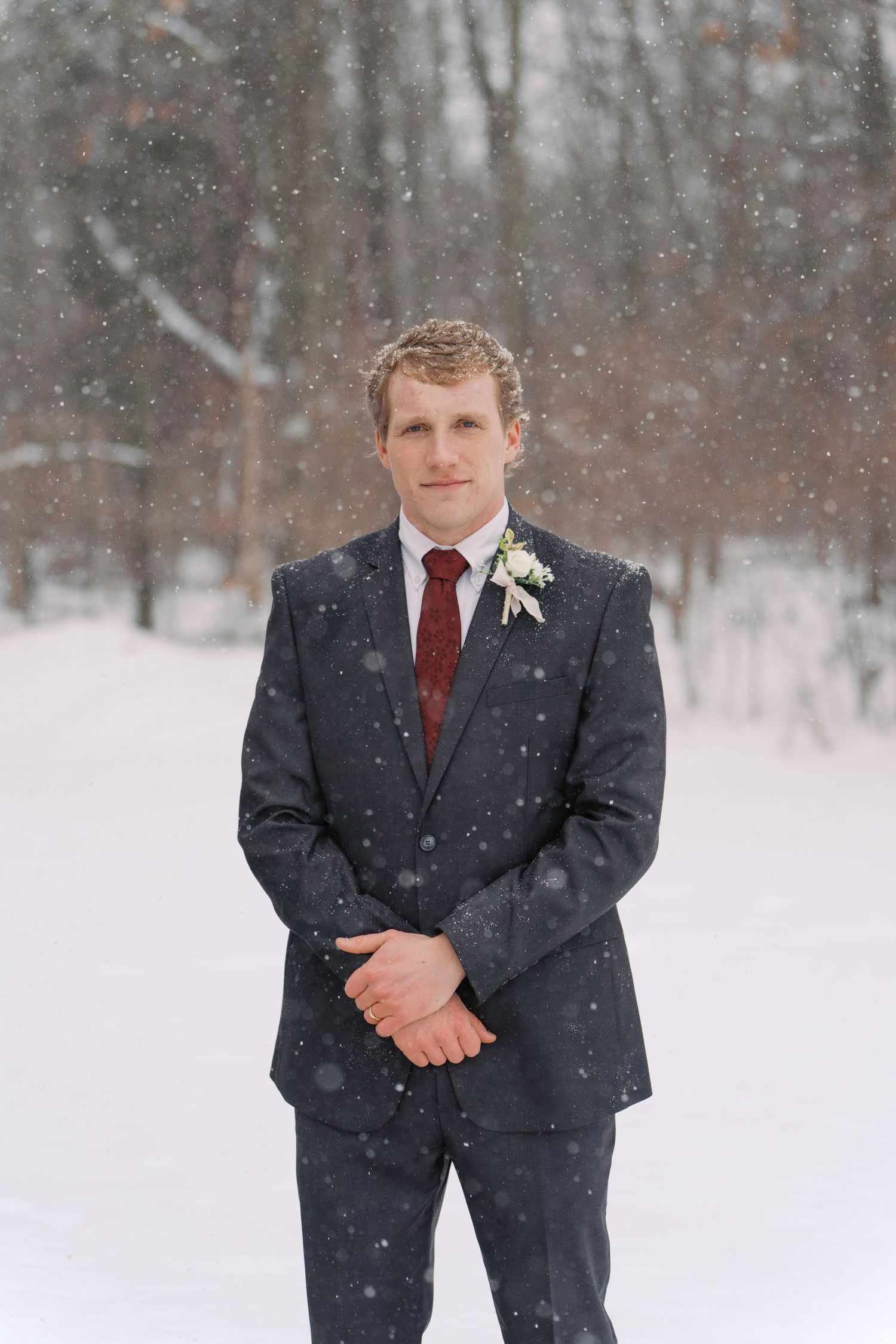 Winter wedding portraits of groom in navy suit against snowy landscape.