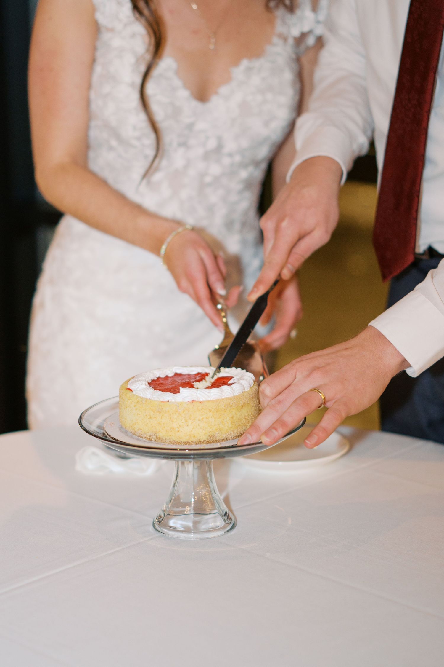 Hands cutting and serving wedding cake on a glass cake stand.