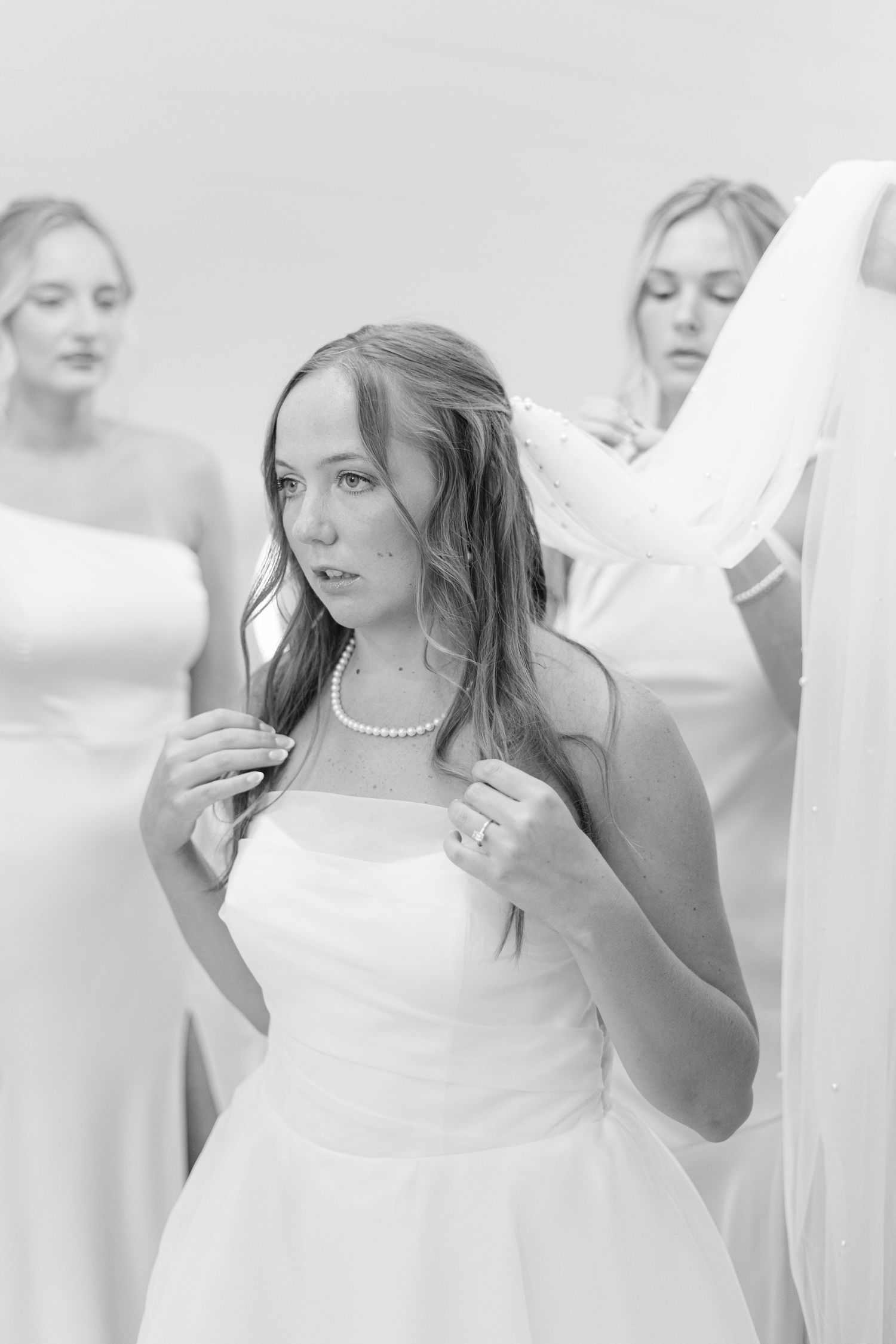 A woman in a white wedding dress smiles while getting ready in a bright room.