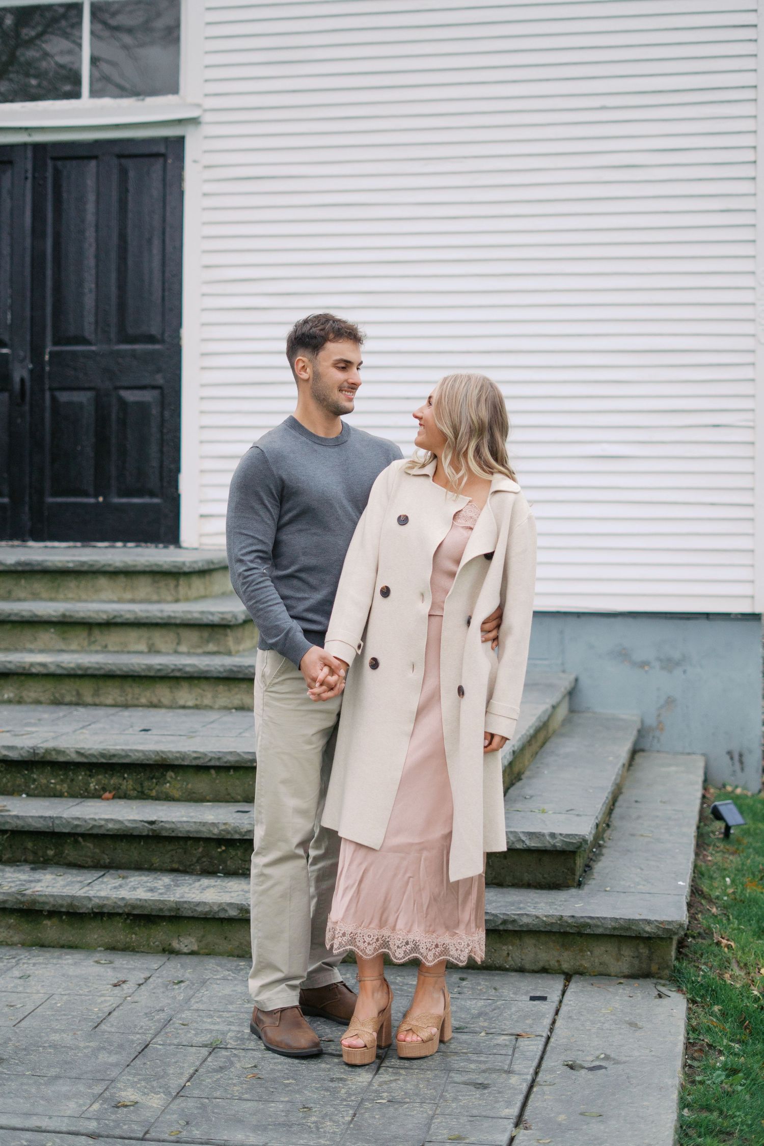 A couple shares a happy moment on stone steps in front of a white building.