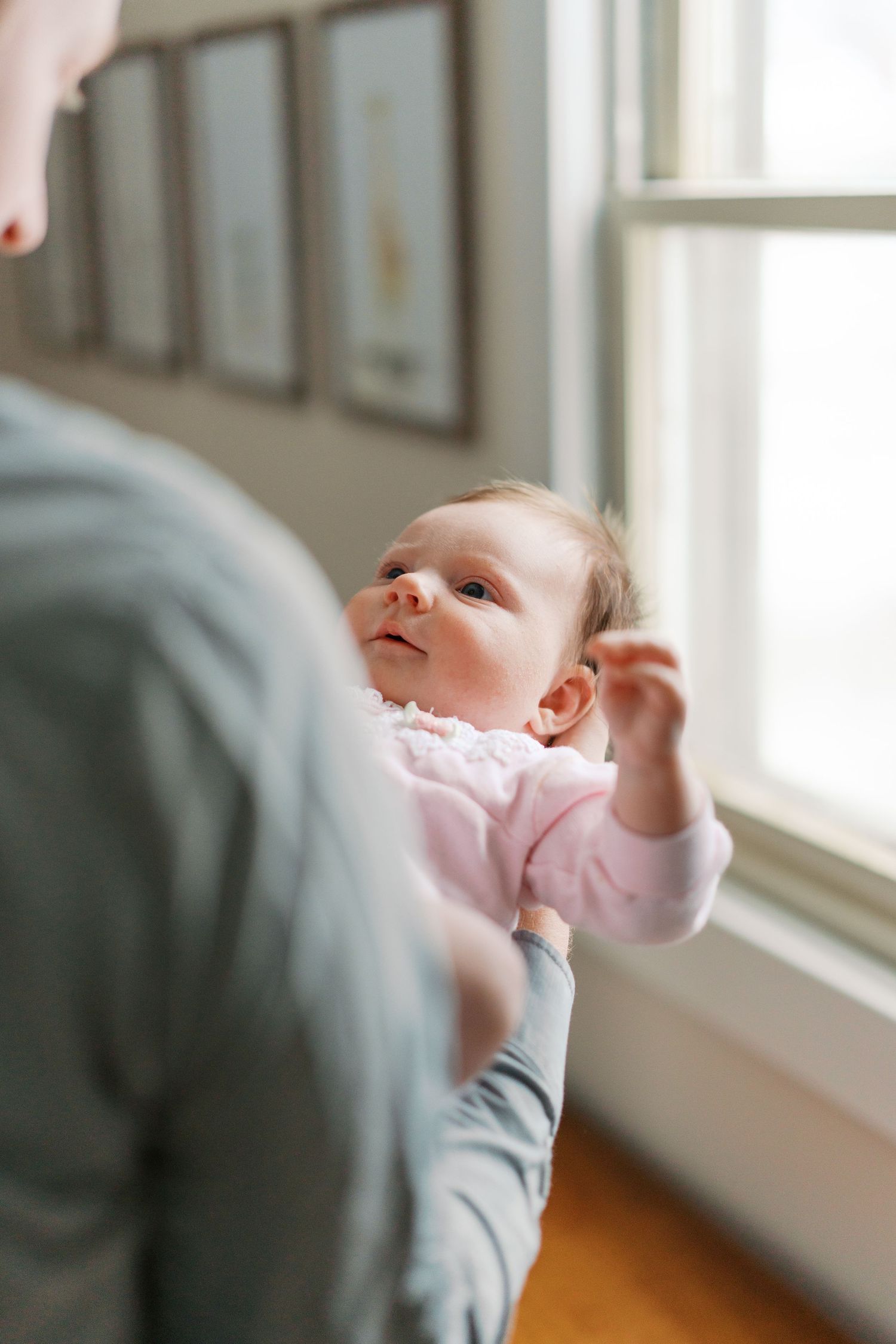 Newborn baby in pink onesie lying down in soft natural window light.