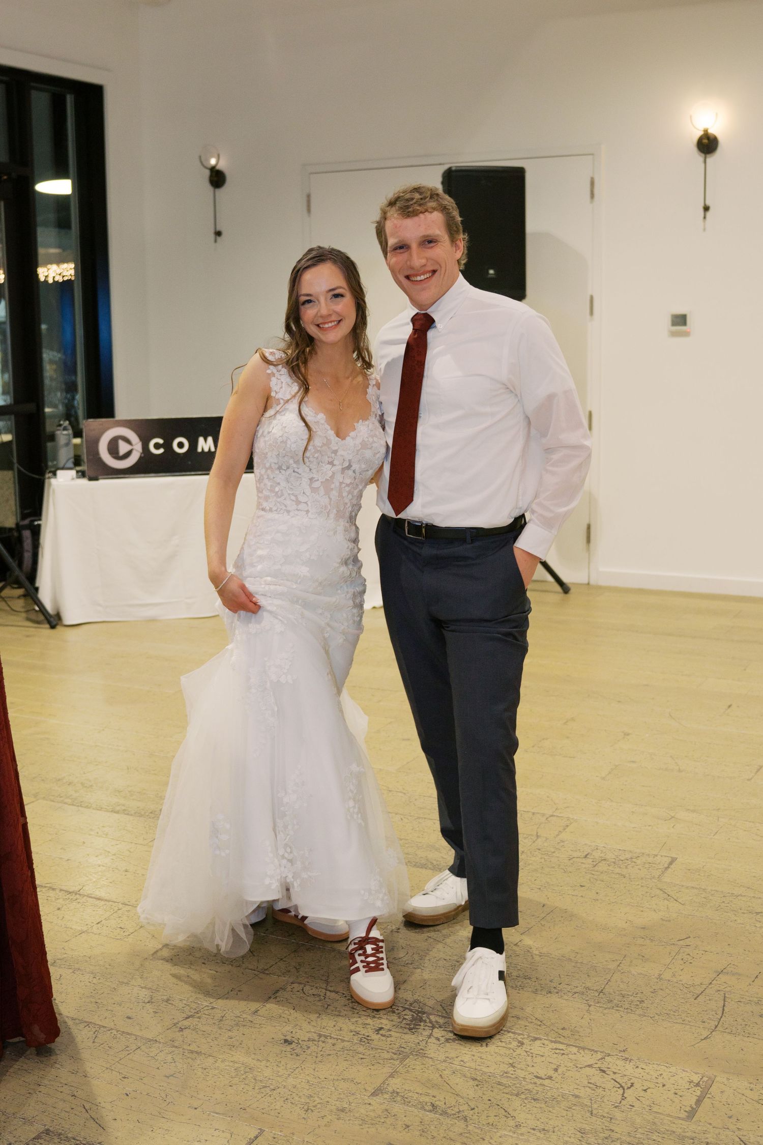 A couple dancing together in a white wedding dress and formal attire on a light-colored dance floor.