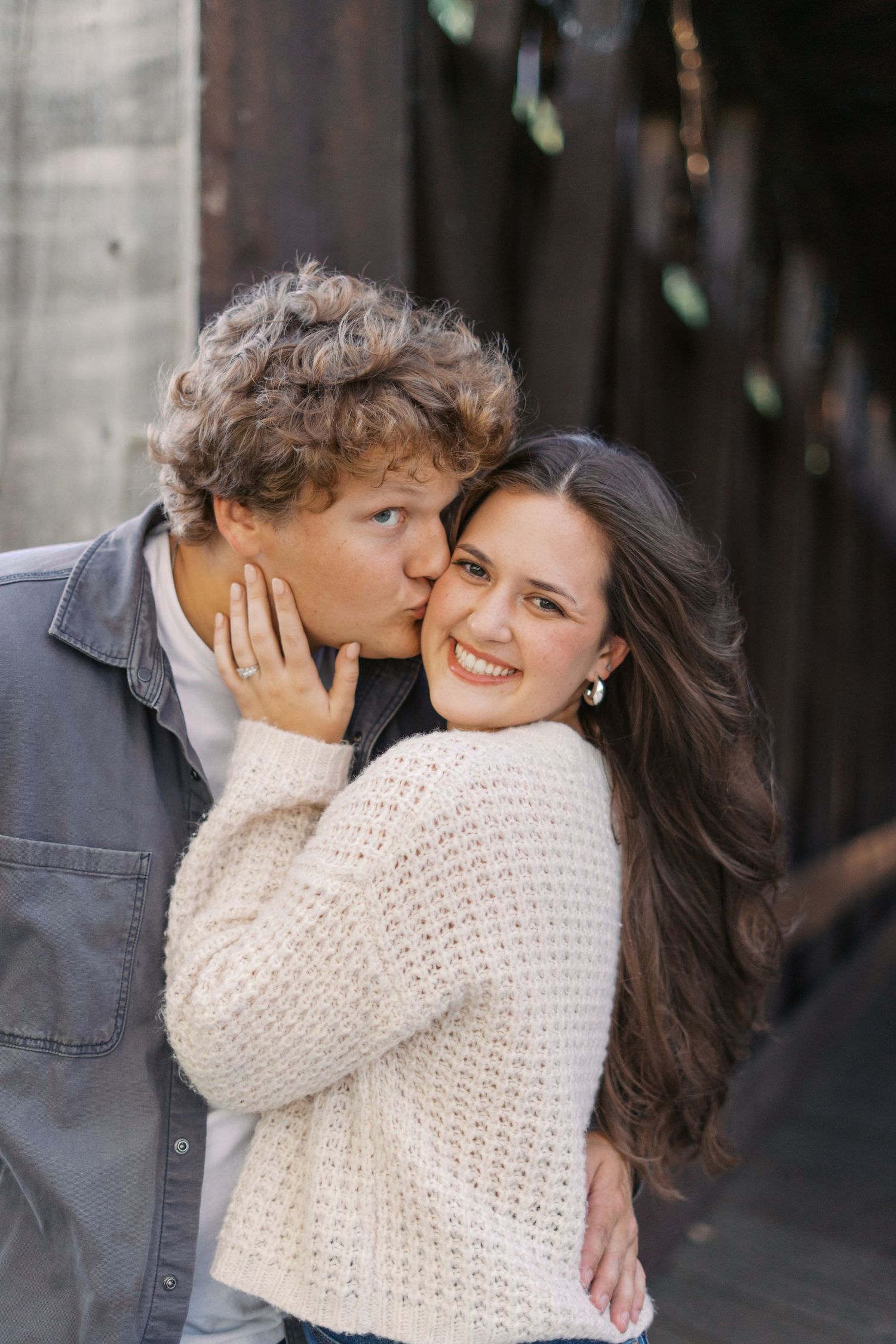 Romantic couple embracing while wearing cream sweater and denim jacket on dark background.