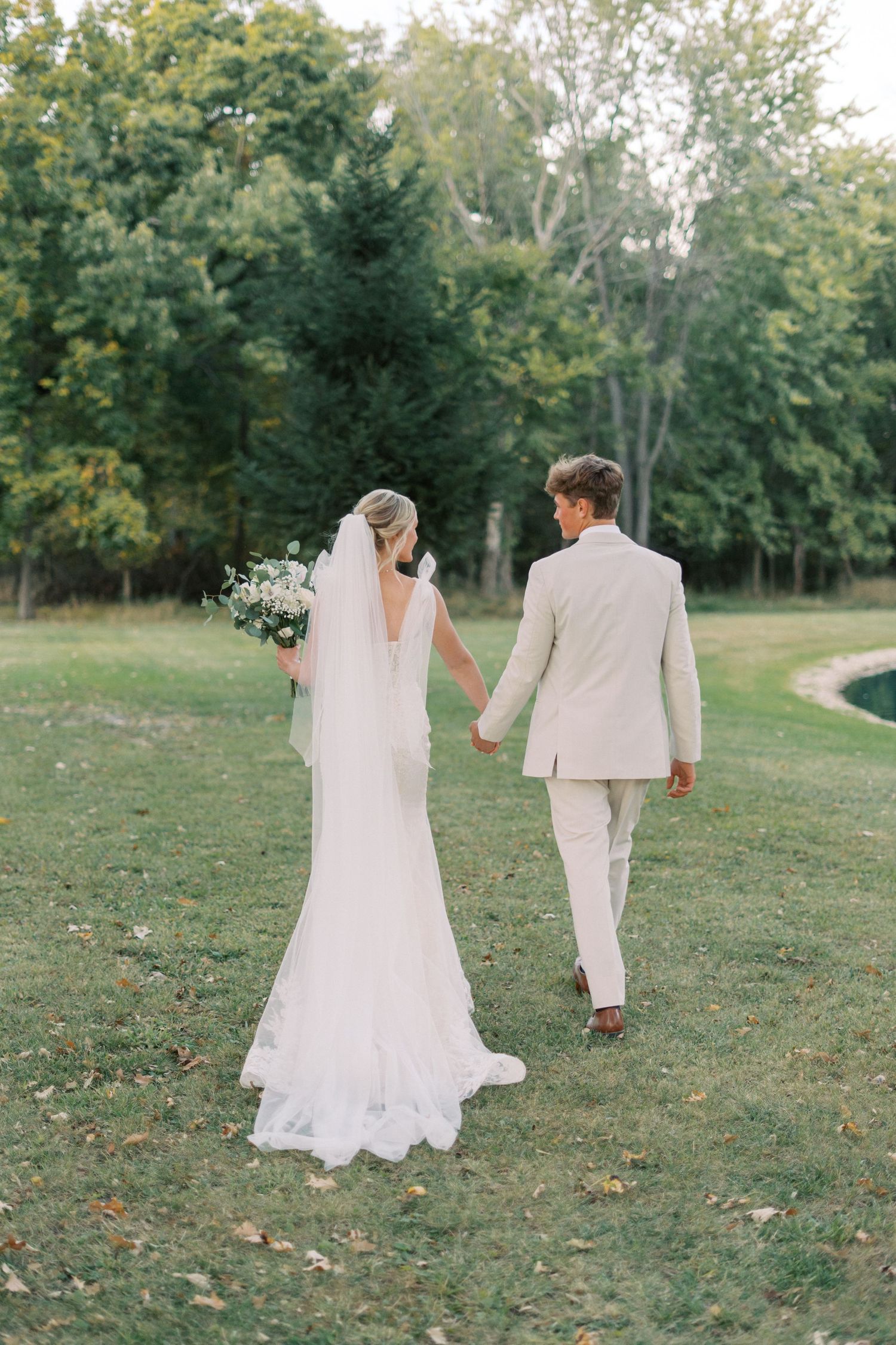 Bride and groom walking through lush garden path in elegant wedding attire.