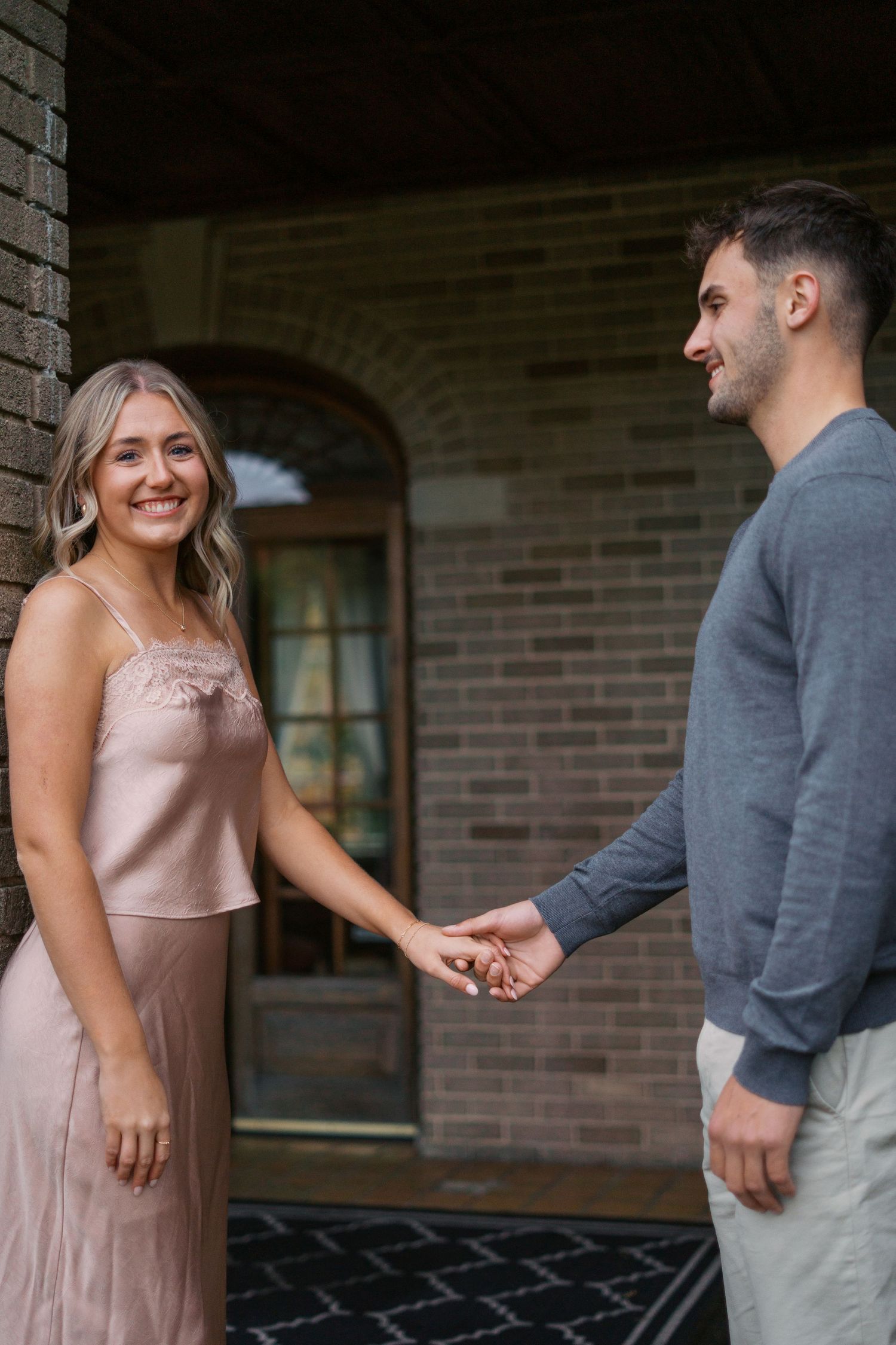 Two people share an intimate moment in front of a brick building wearing pink and grey.