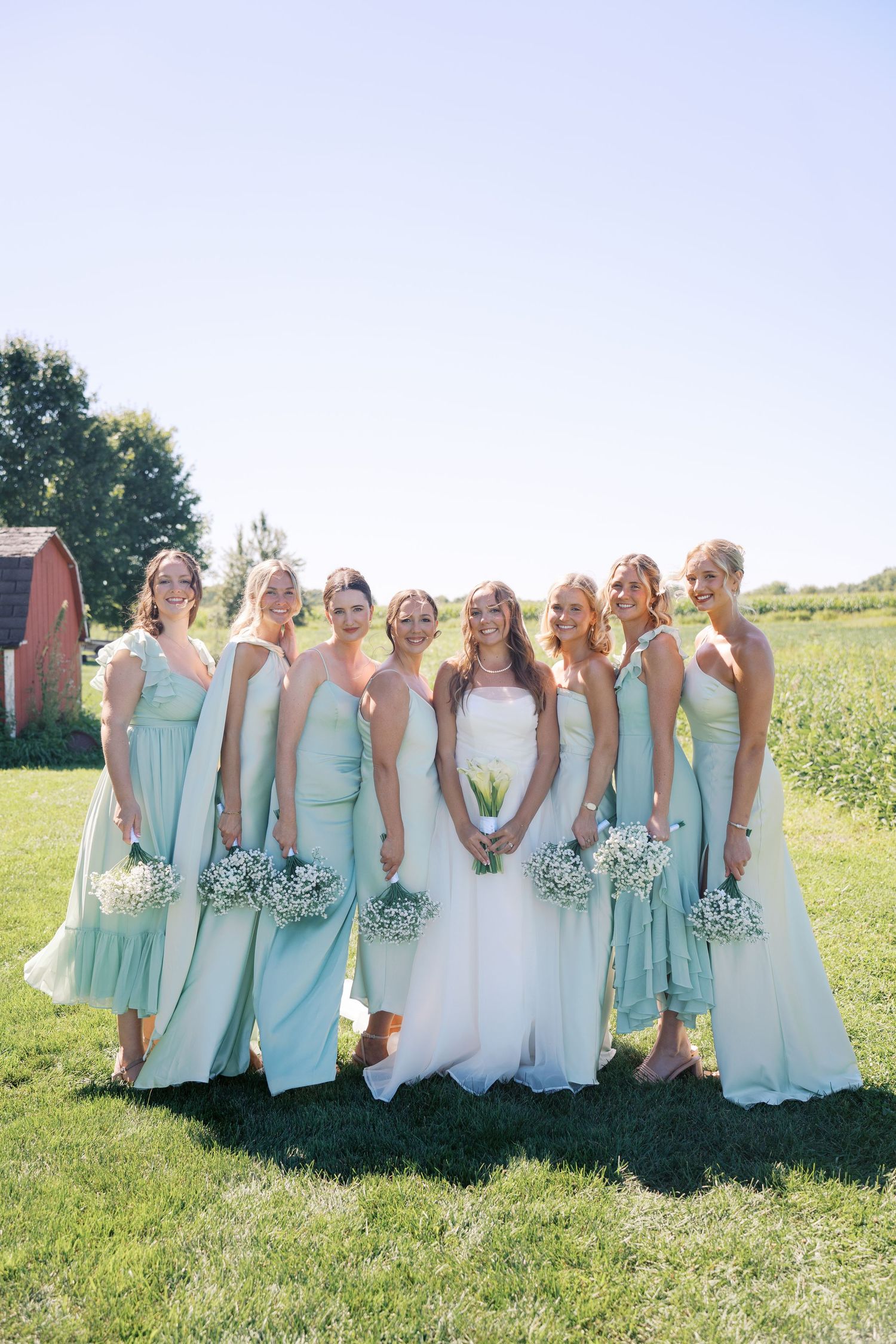 Bridesmaids in mint green dresses stand with the bride in white for an outdoor wedding photo.