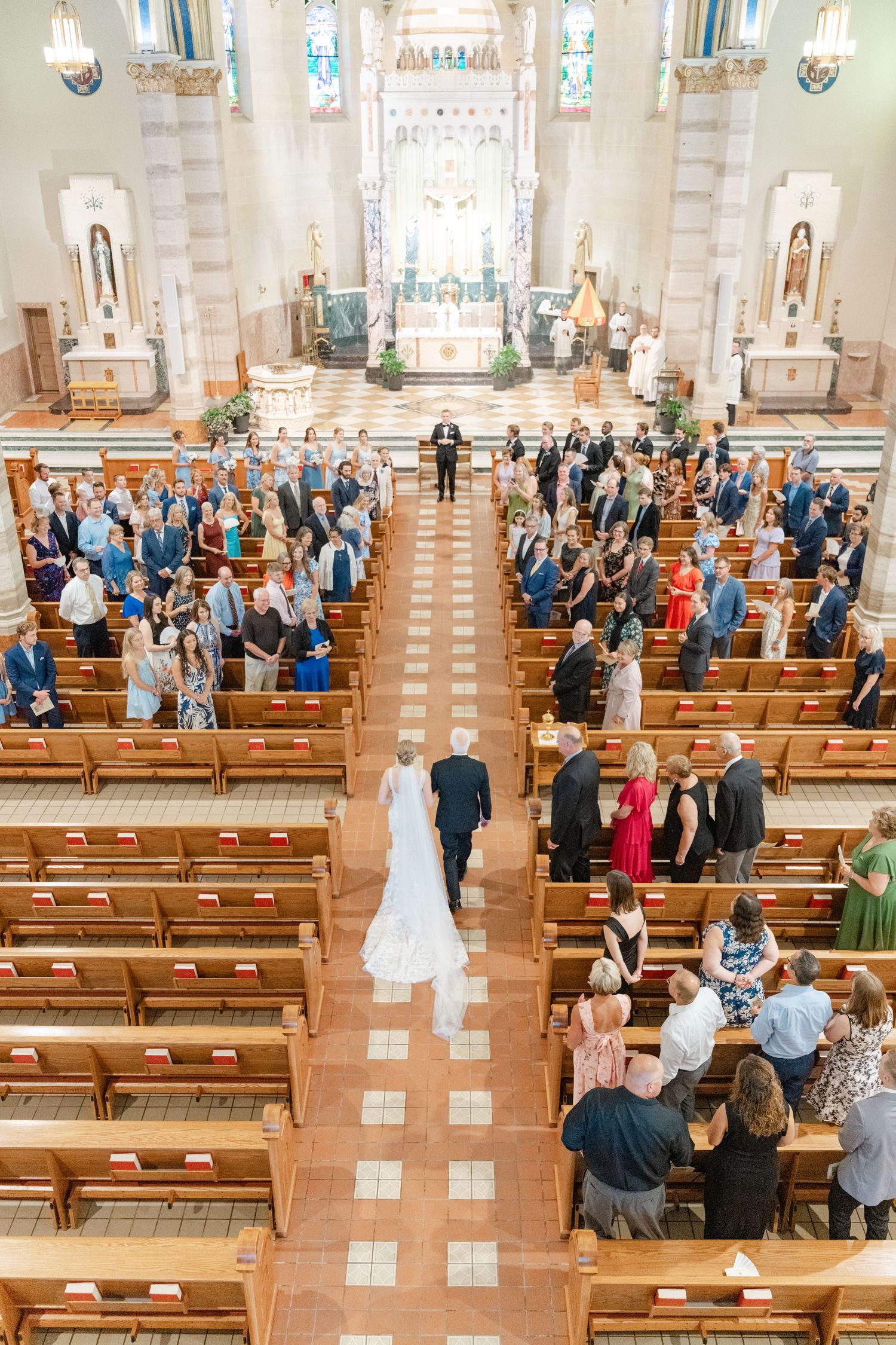 Wedding ceremony in progress inside traditional church with guests seated in wooden pews.