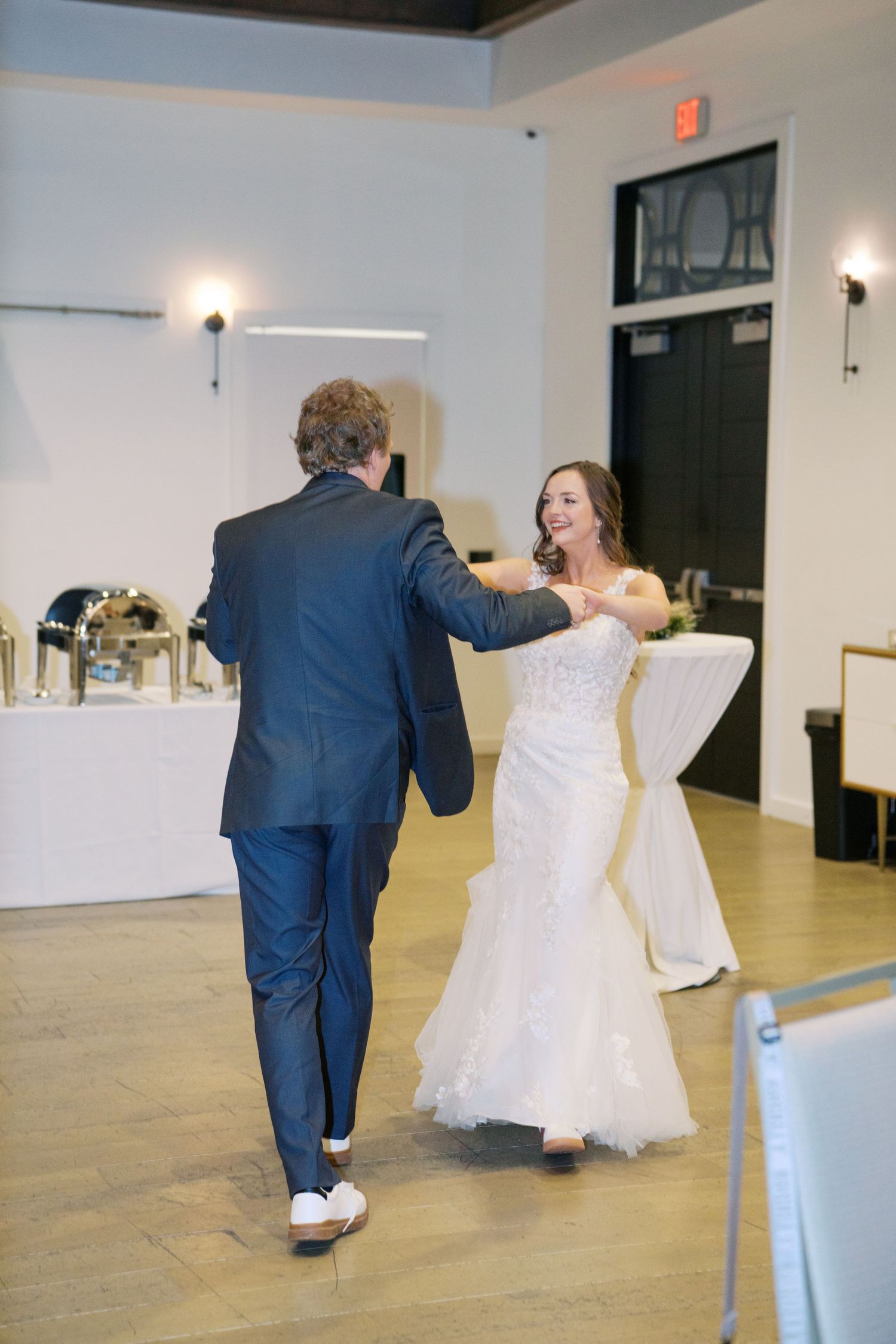 A couple performs a lively dance routine in a spacious reception venue with white walls.