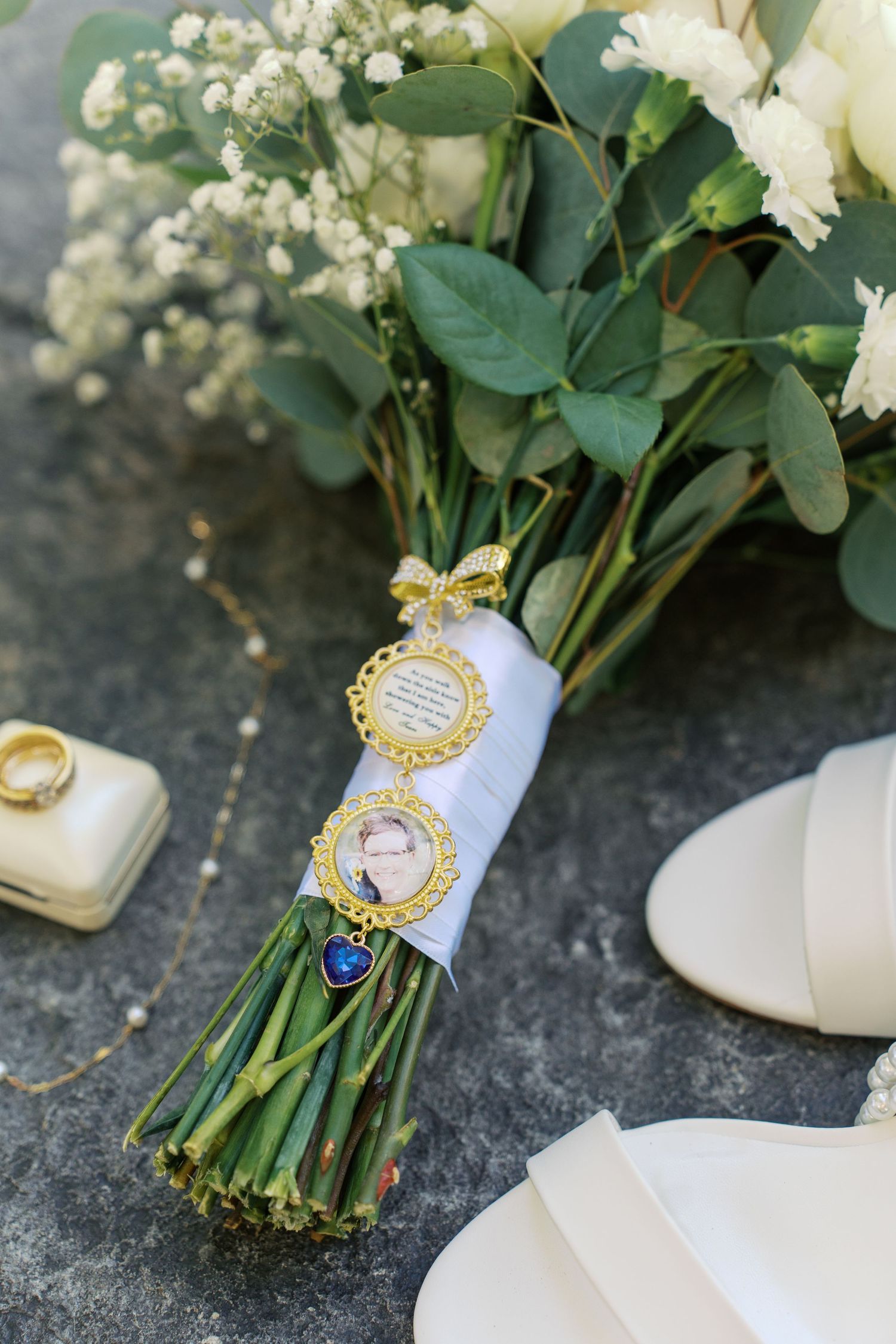 White rose bouquet with sentimental charms and family photos attached to stems.