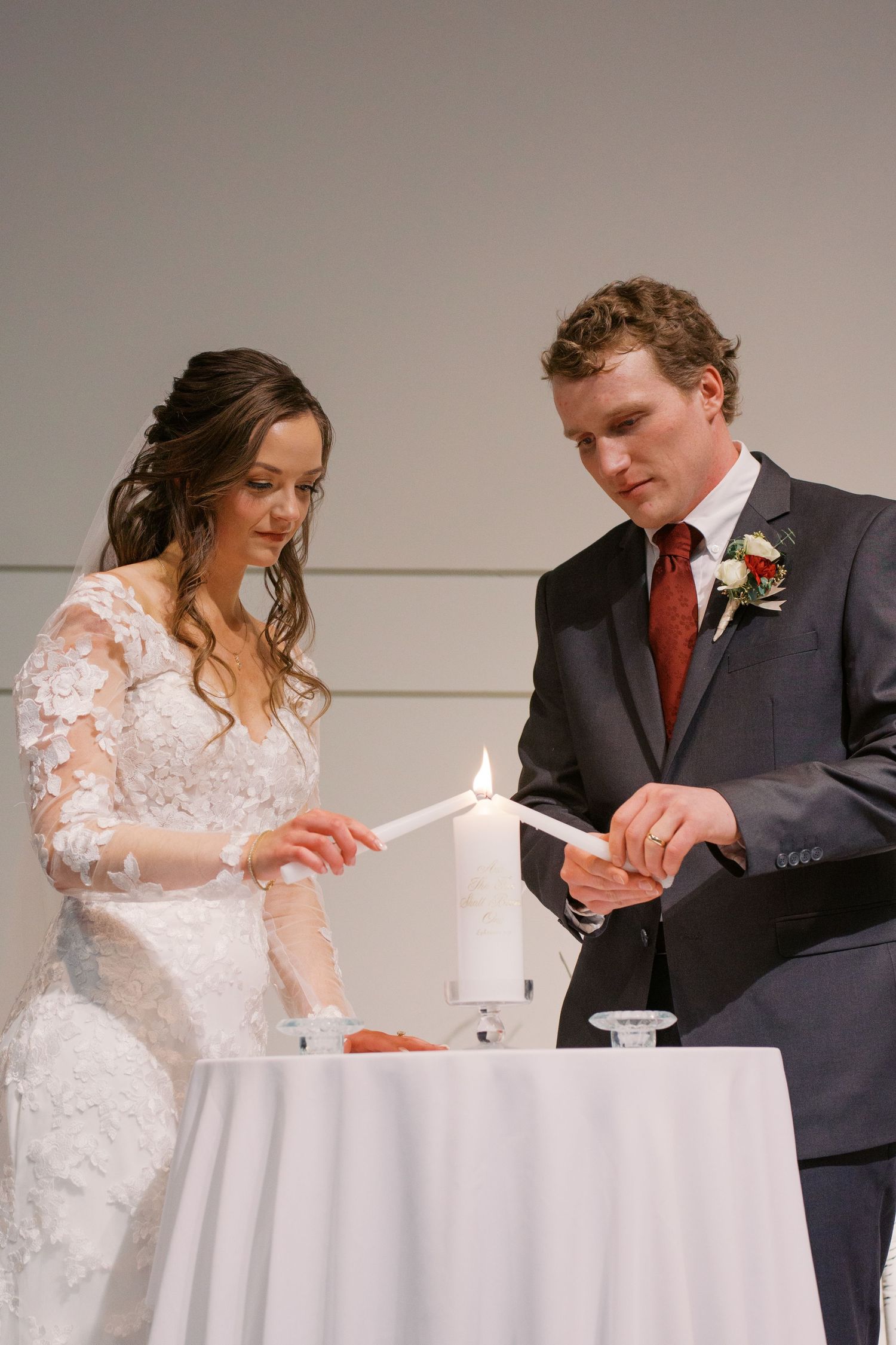 A couple performs a unity candle ceremony at their wedding with a white tablecloth.