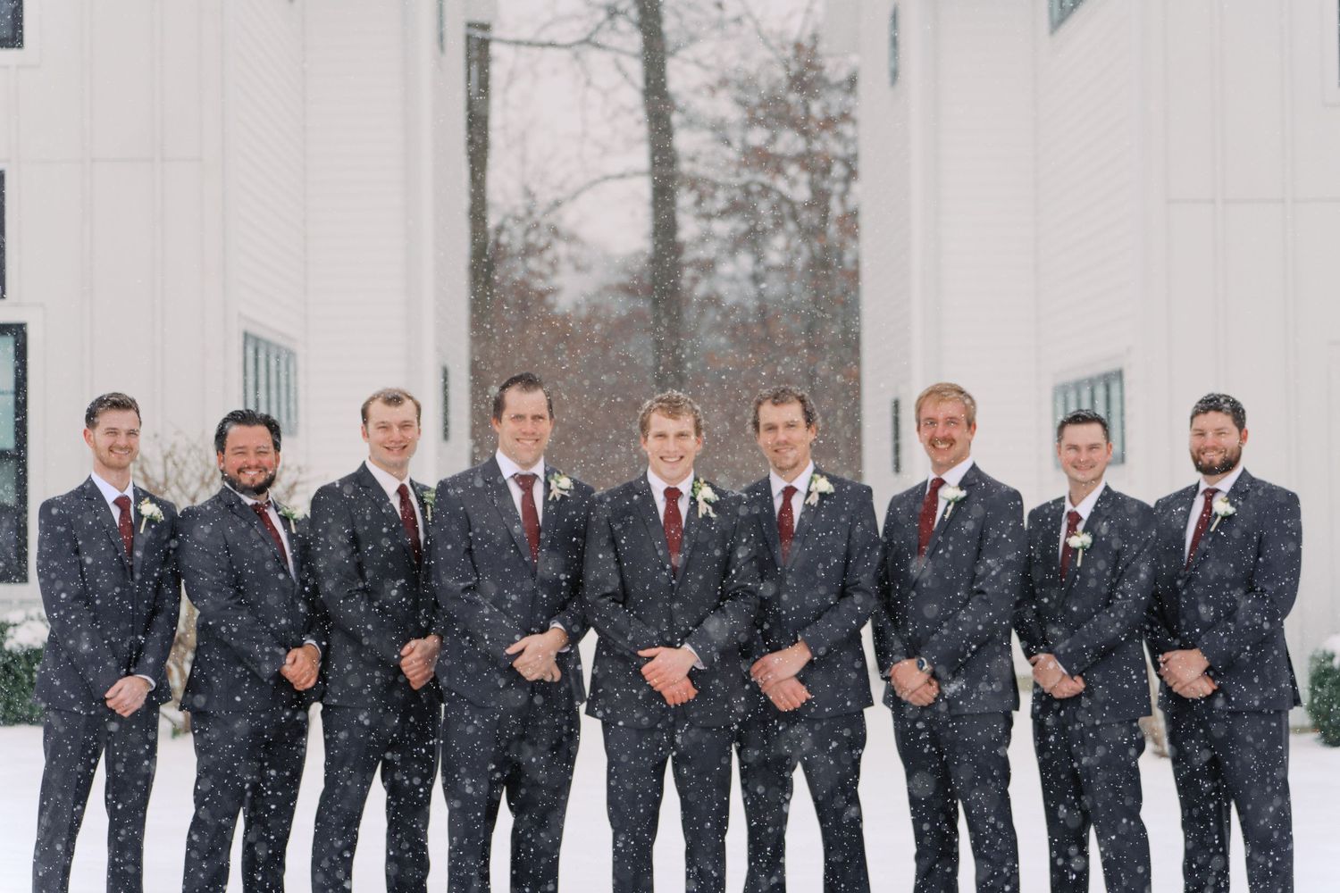 Groomsmen in matching suits pose in snowy winter setting.