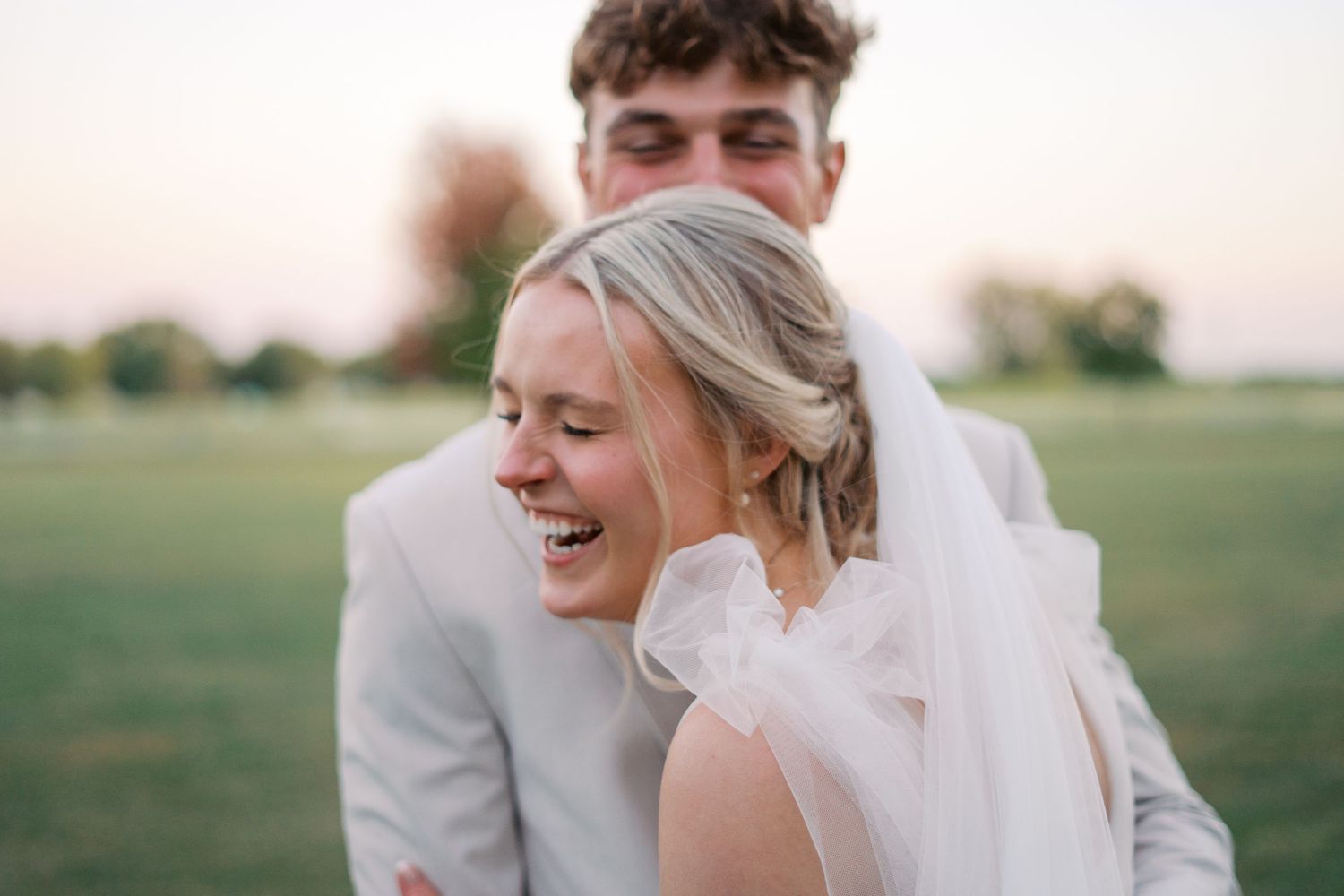 Joyful wedding couple embracing in an outdoor field at sunset.