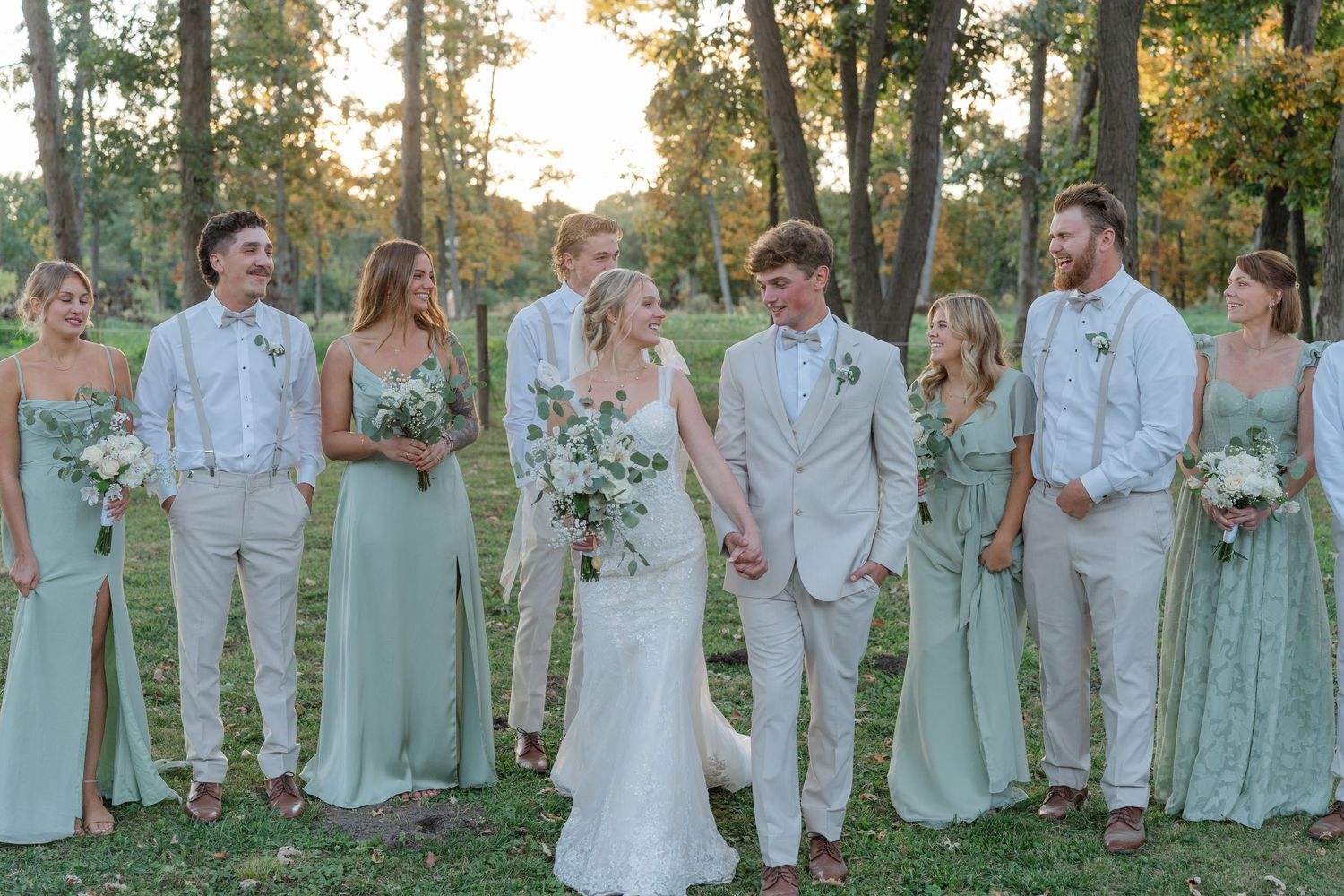 Wedding party in mint green dresses and cream suits poses together outdoors.