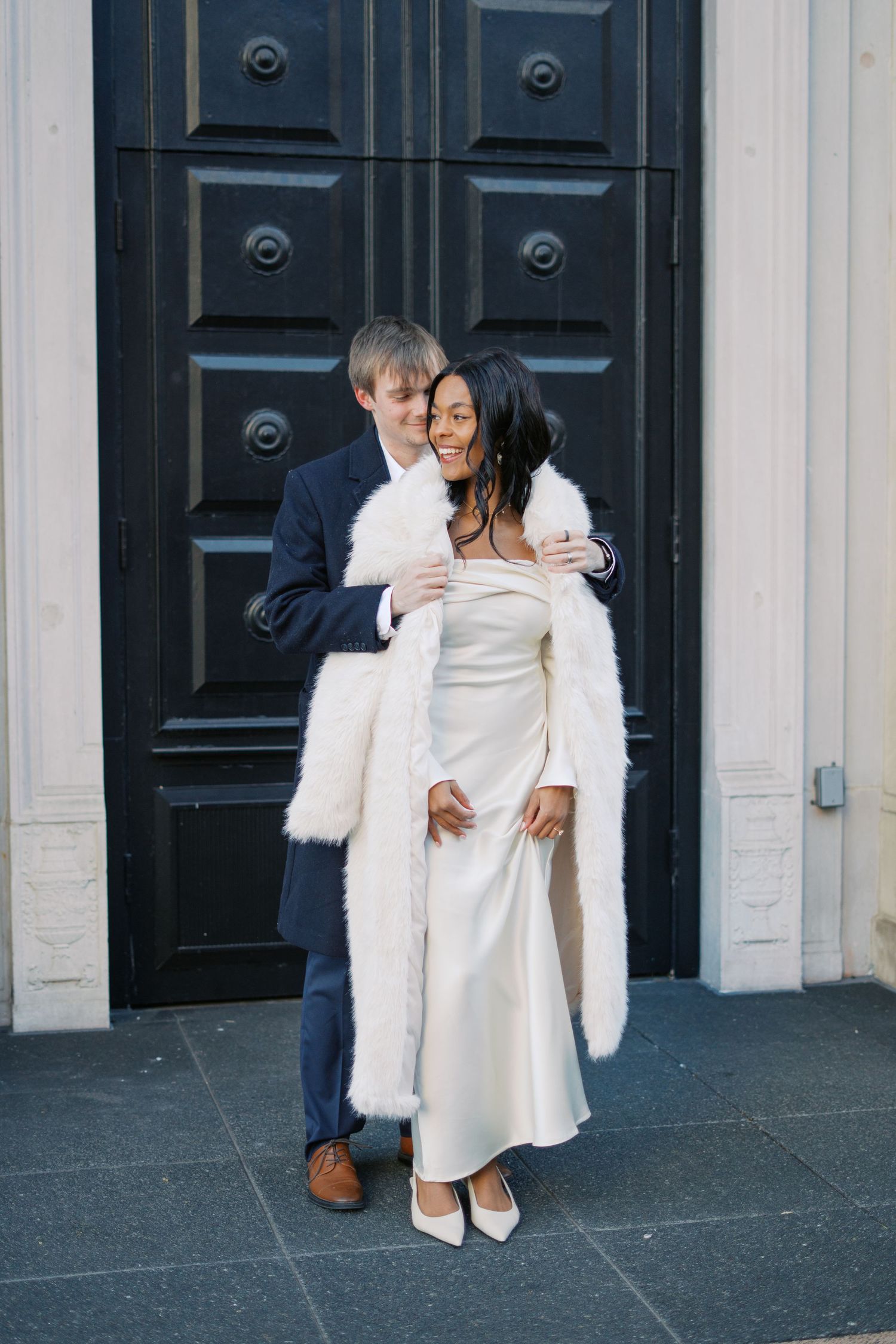 Wedding couple shares playful moments against architectural backdrop.
