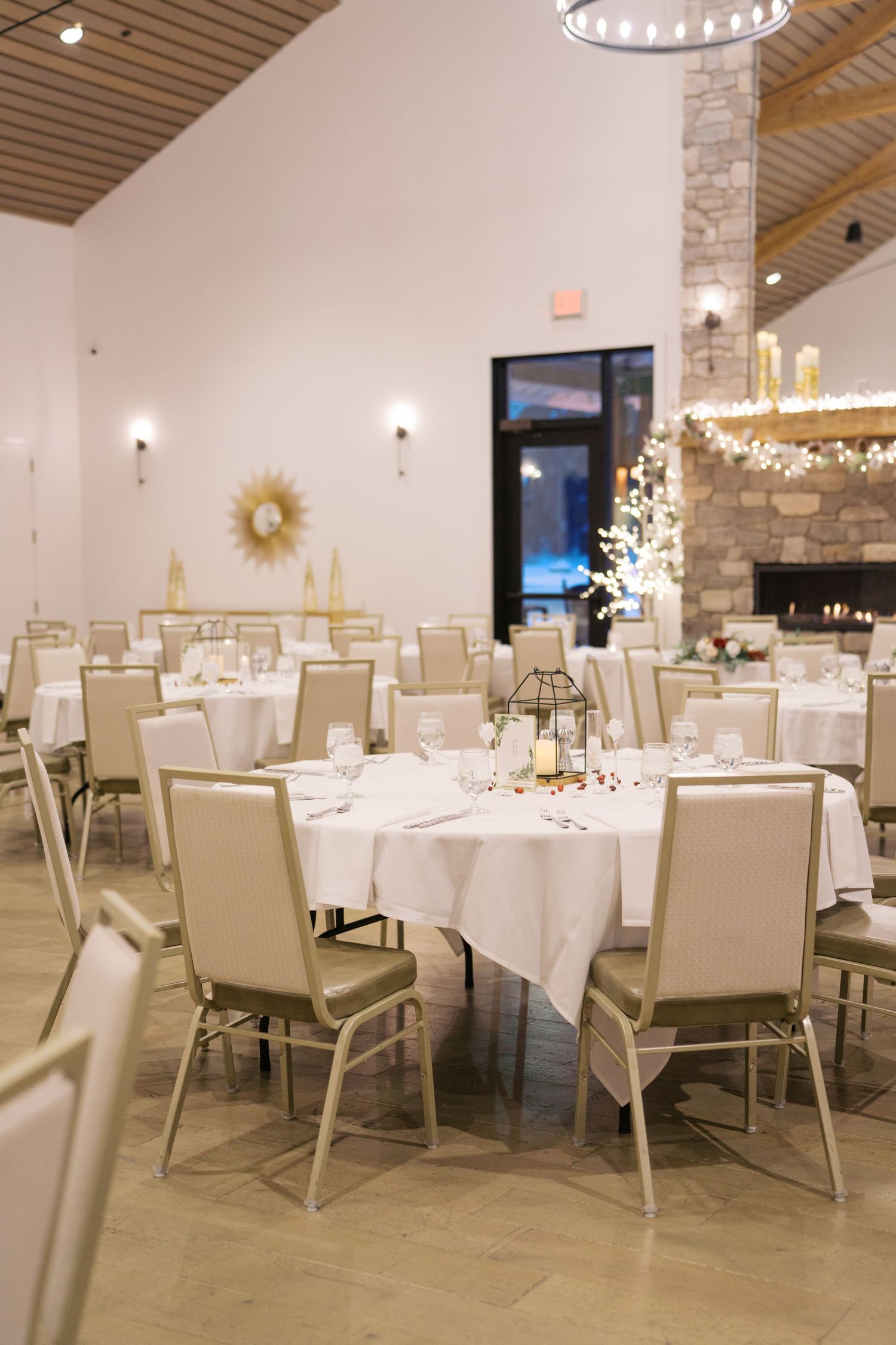 Elegant wedding reception venue with white tablecloths, cream chairs, and warm lighting.