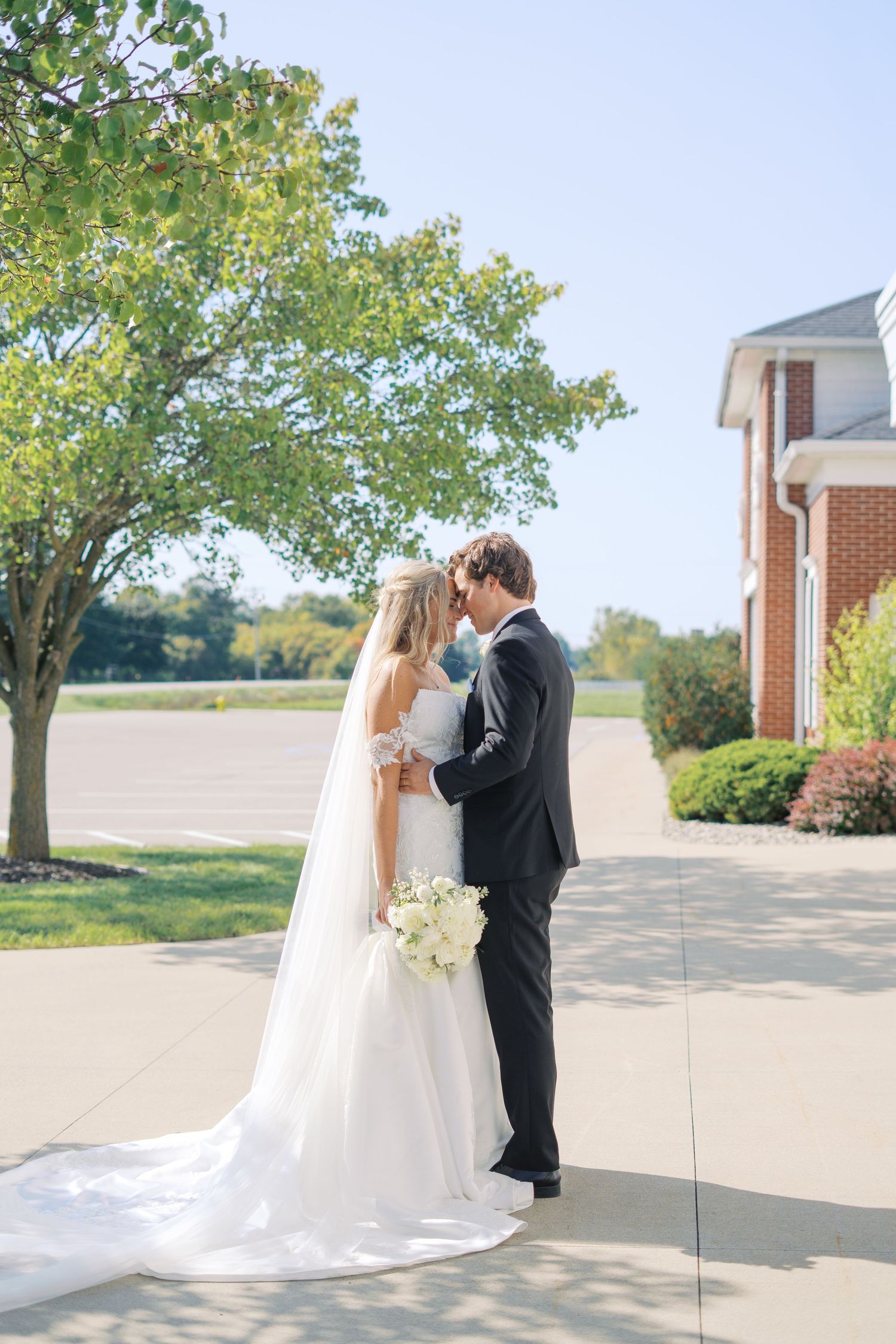 Sunny outdoor wedding portrait with couple embracing near brick church building.