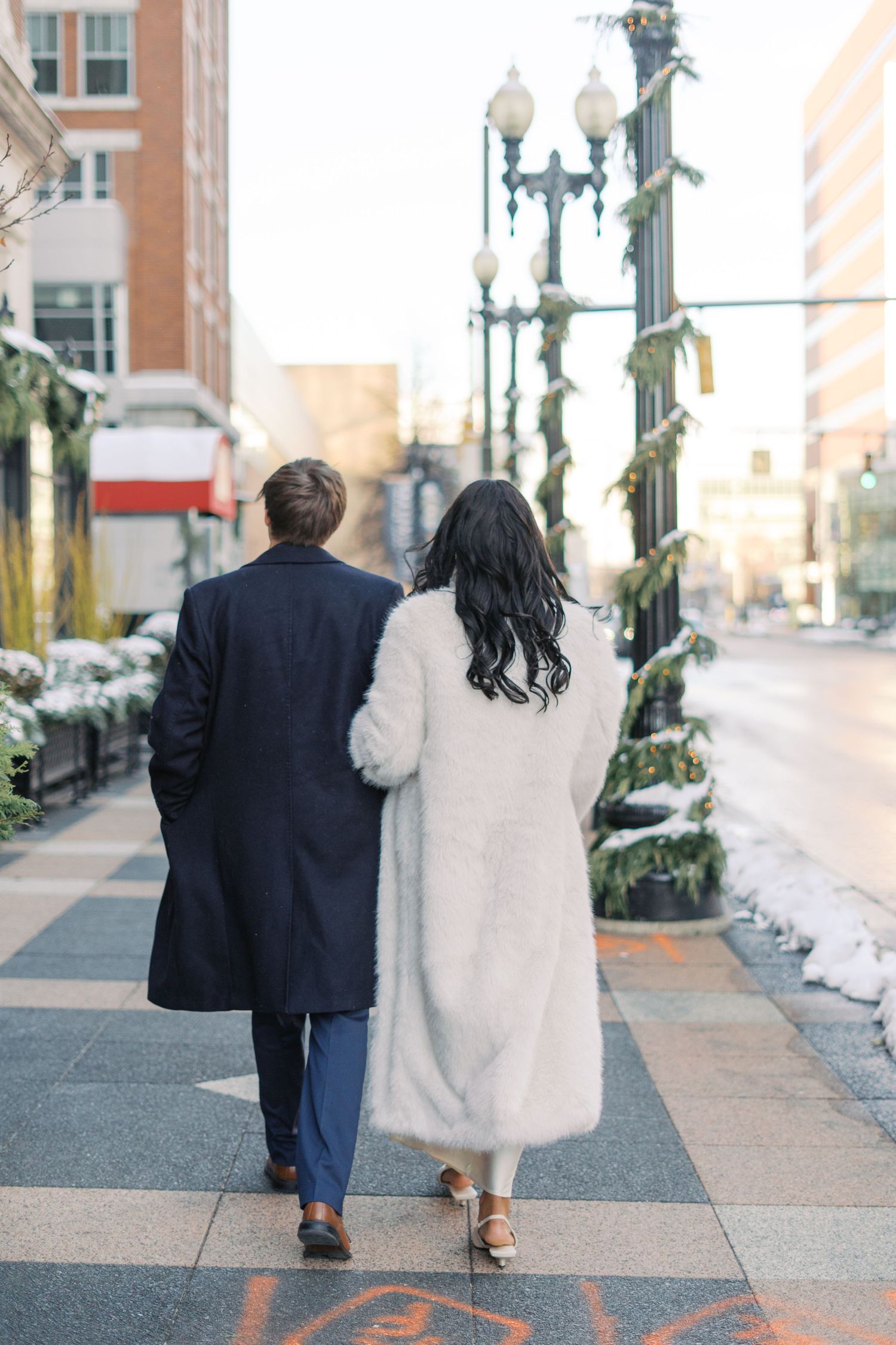 Couple walking hand in hand down an urban sidewalk with decorative street lamps.