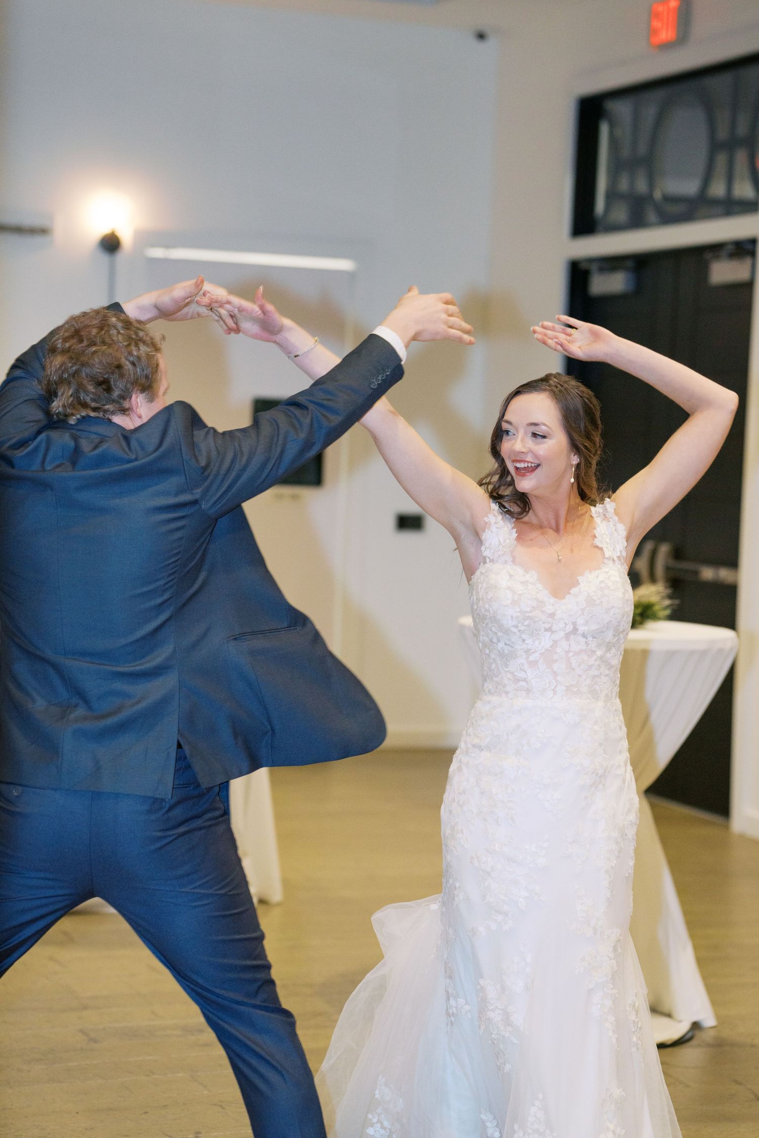 A joyful couple dances energetically in a reception hall with white walls and hardwood floors.
