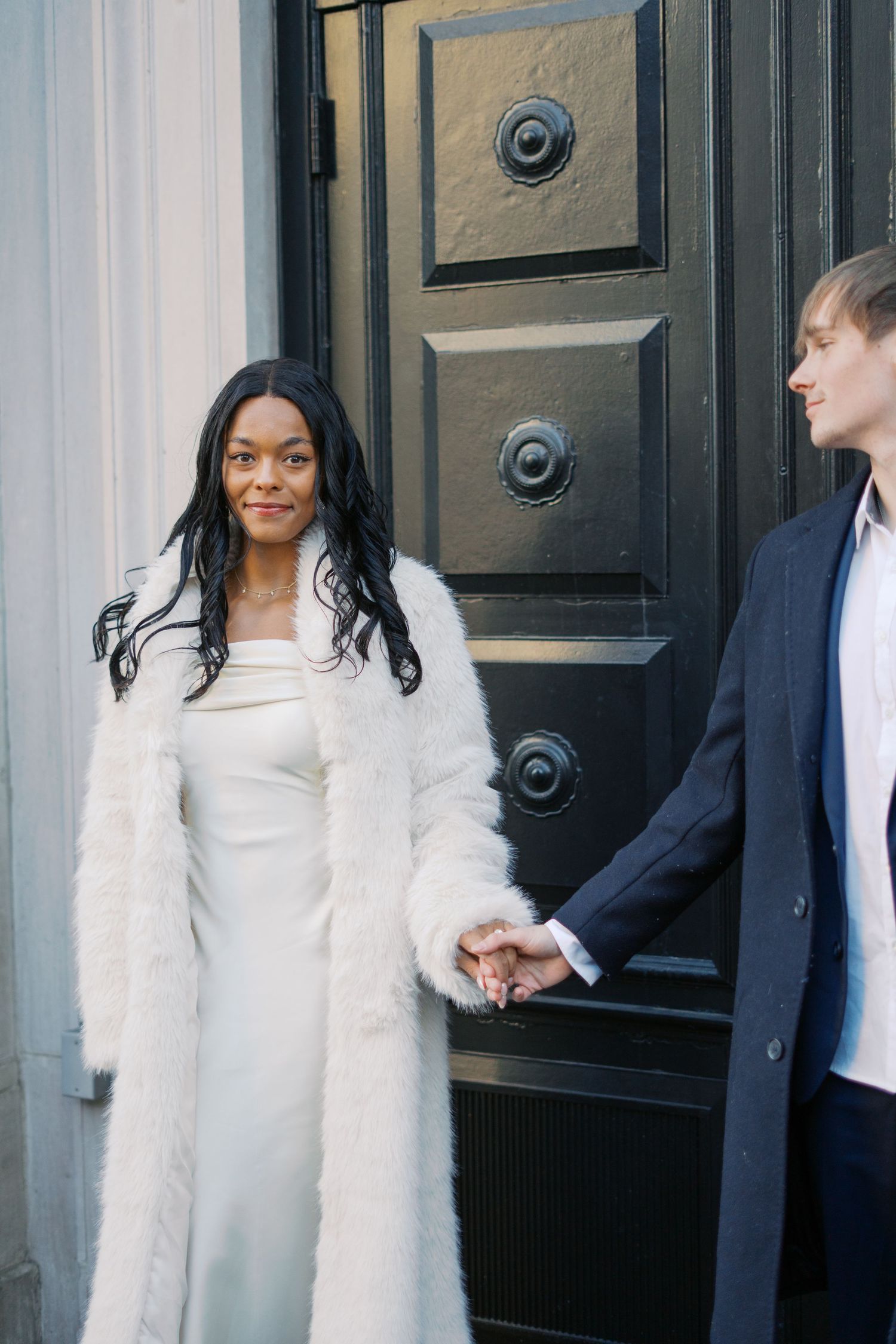 Couple shares joyful moments while posing against a black door in formal attire.