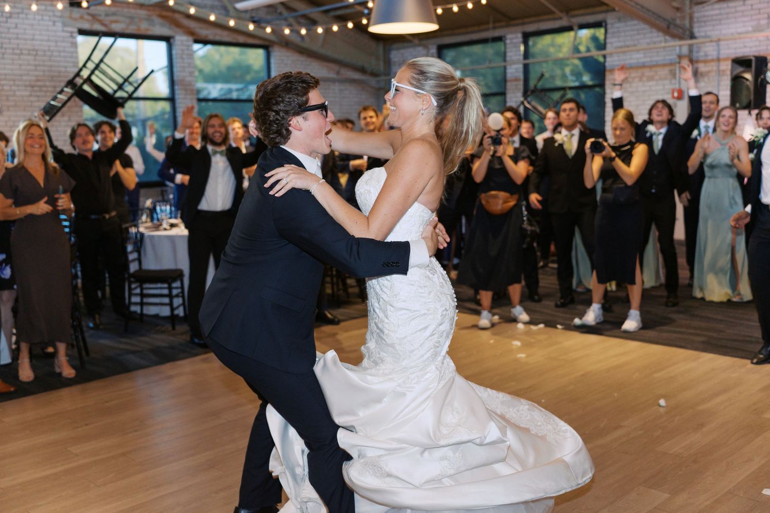 Wedding guests dance and celebrate on a wooden dance floor under string lights.