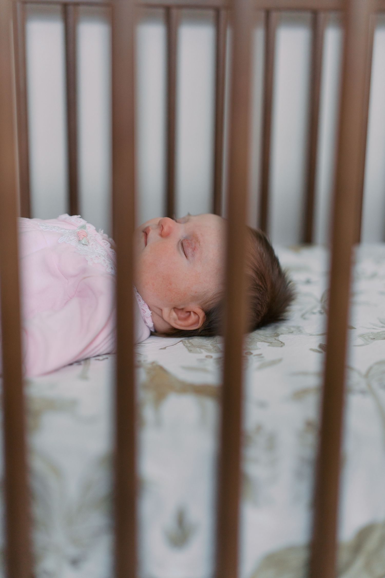 Baby in pink outfit sleeping peacefully in wooden crib.